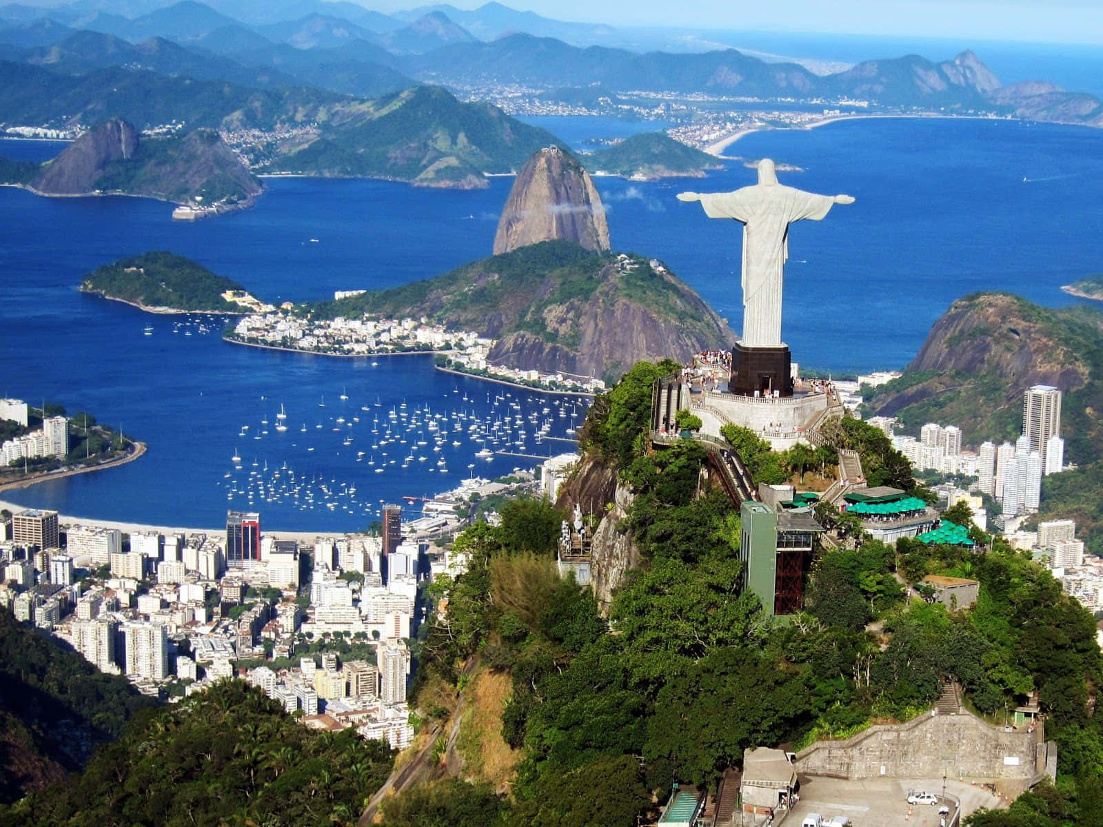 Brazil 桌布 壁紙 — 基督救世主雕像俯瞰著里約熱內盧充滿活力的海灣和城市景觀，天空湛藍。