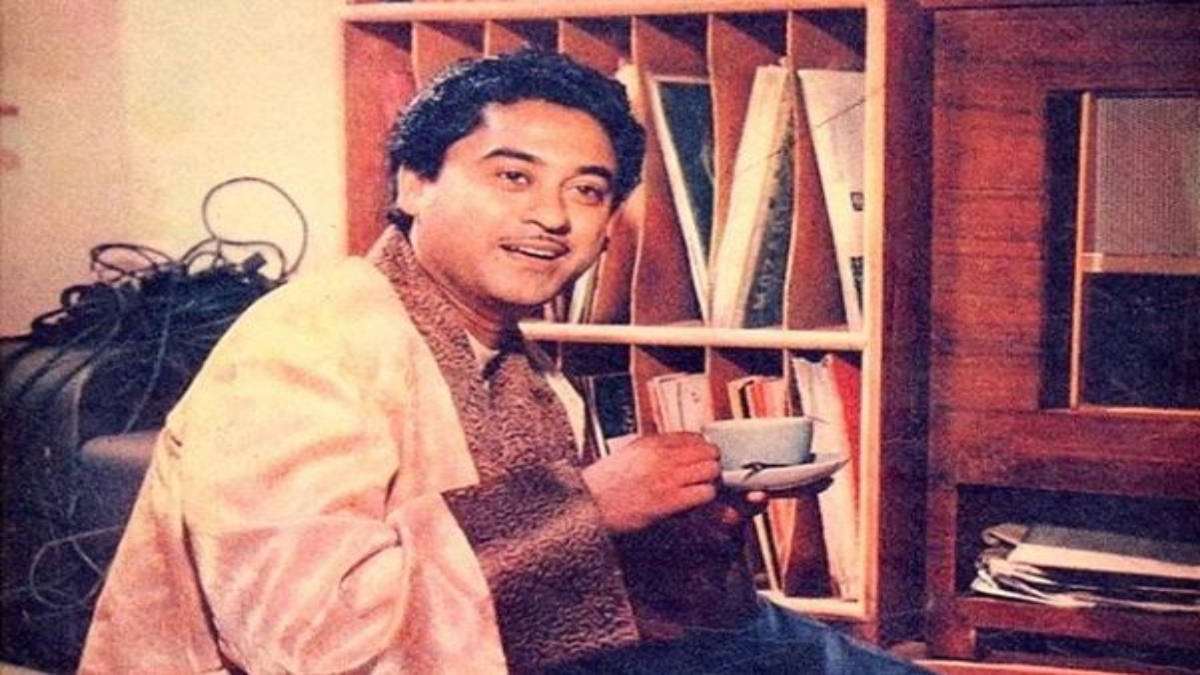 男人微笑，在溫暖的室內環境中手持茶杯，旁邊有書架。