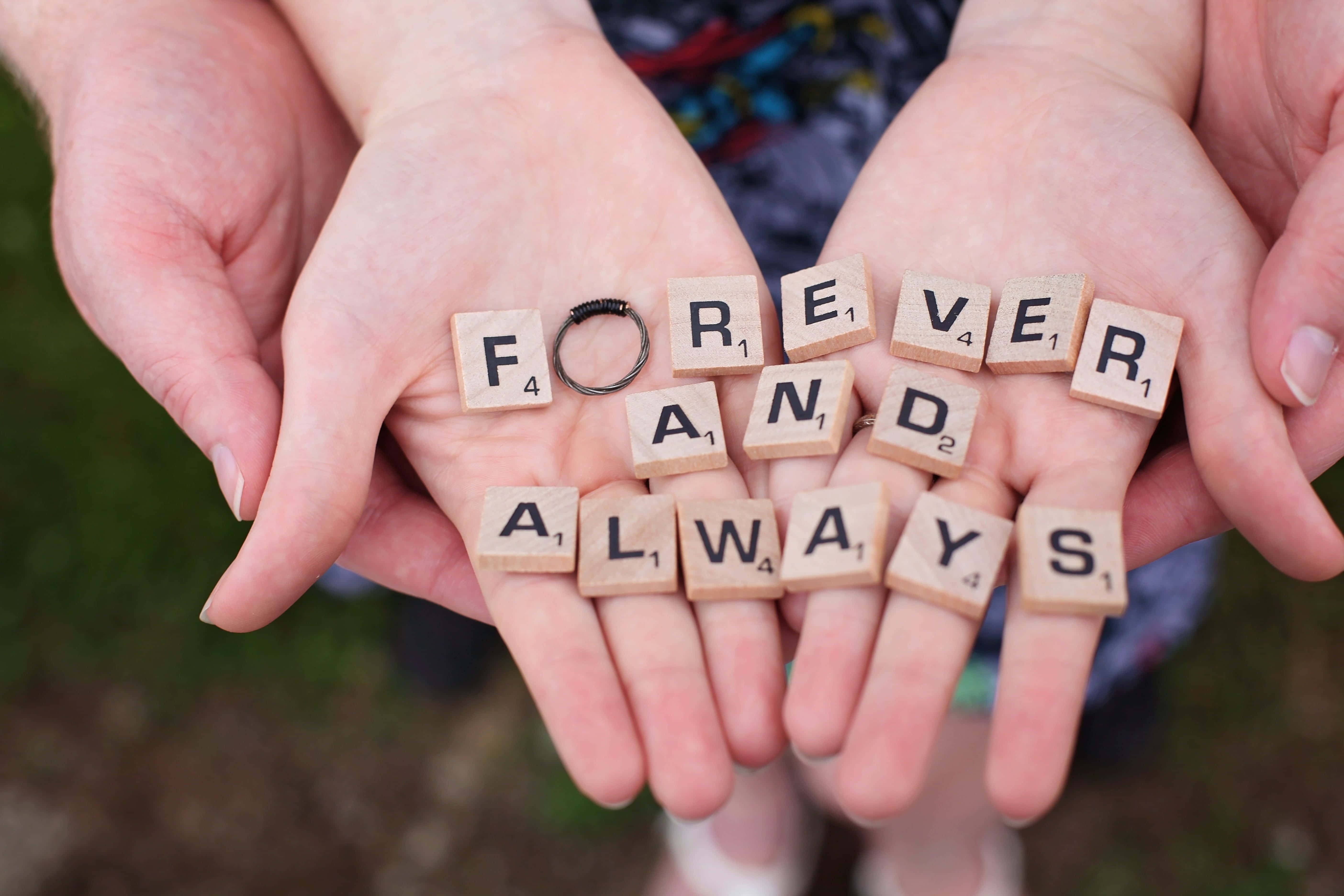 堅定愛意手部圖 壁紙 — 兩隻手捧著木製 Scrabble 字母牌，拼出 forever and always，字母之間放著一枚結婚戒指。