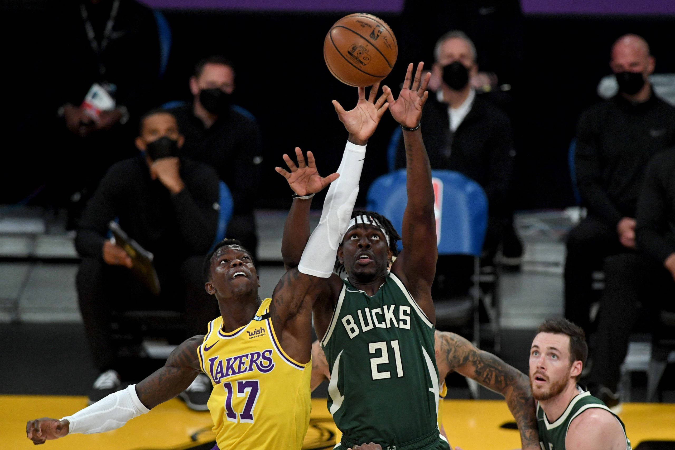 堅定雄鹿隊Jrue Holiday 壁紙 — 兩名籃球運動員在觀眾注視下激烈跳起爭搶籃板球。