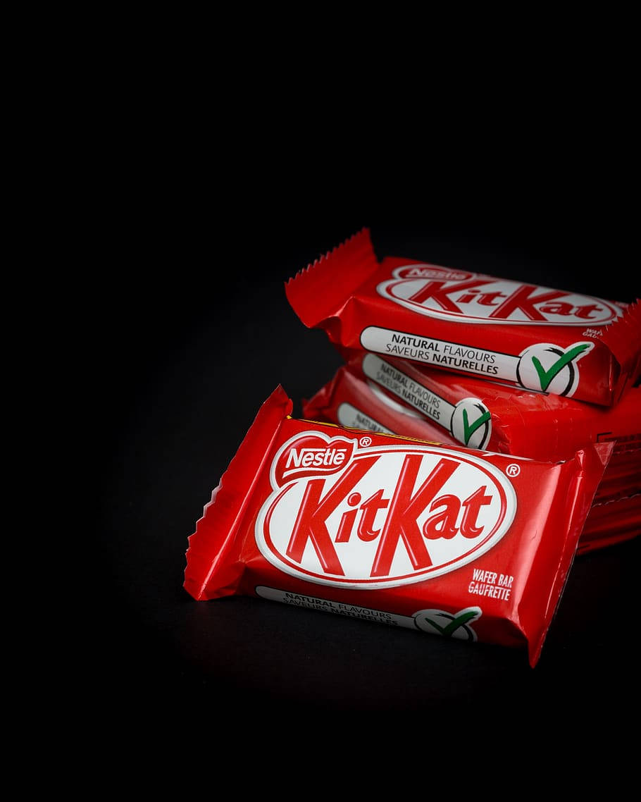 堆疊的 Kit Kat 巧克力 壁紙 — 堆疊的KitKat朱古力棒以鮮紅色包裝在攝影棚燈光下於純黑背景上閃閃發光。