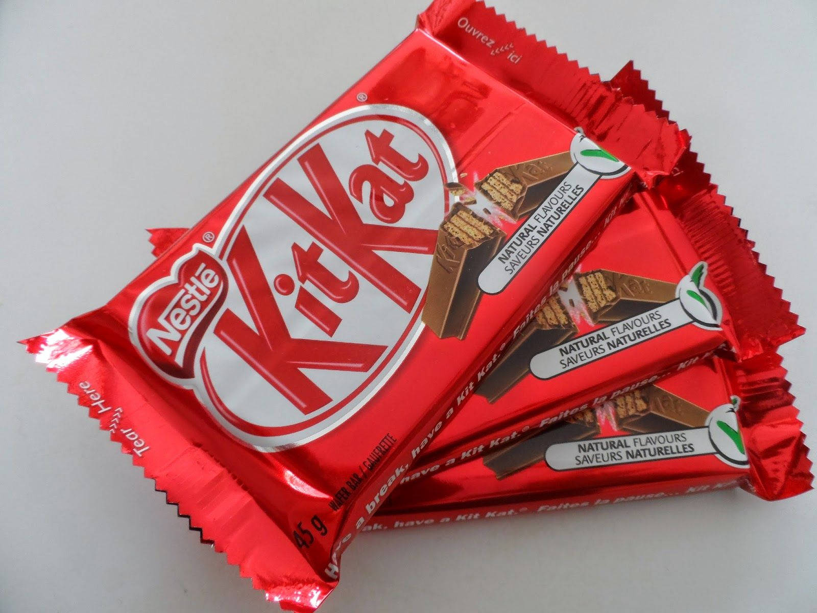 堆疊的紅色 Kit Kat 壁紙 — 三塊紅色錫紙包裝的KitKat朱古力棒對角堆疊在純白色表面上。