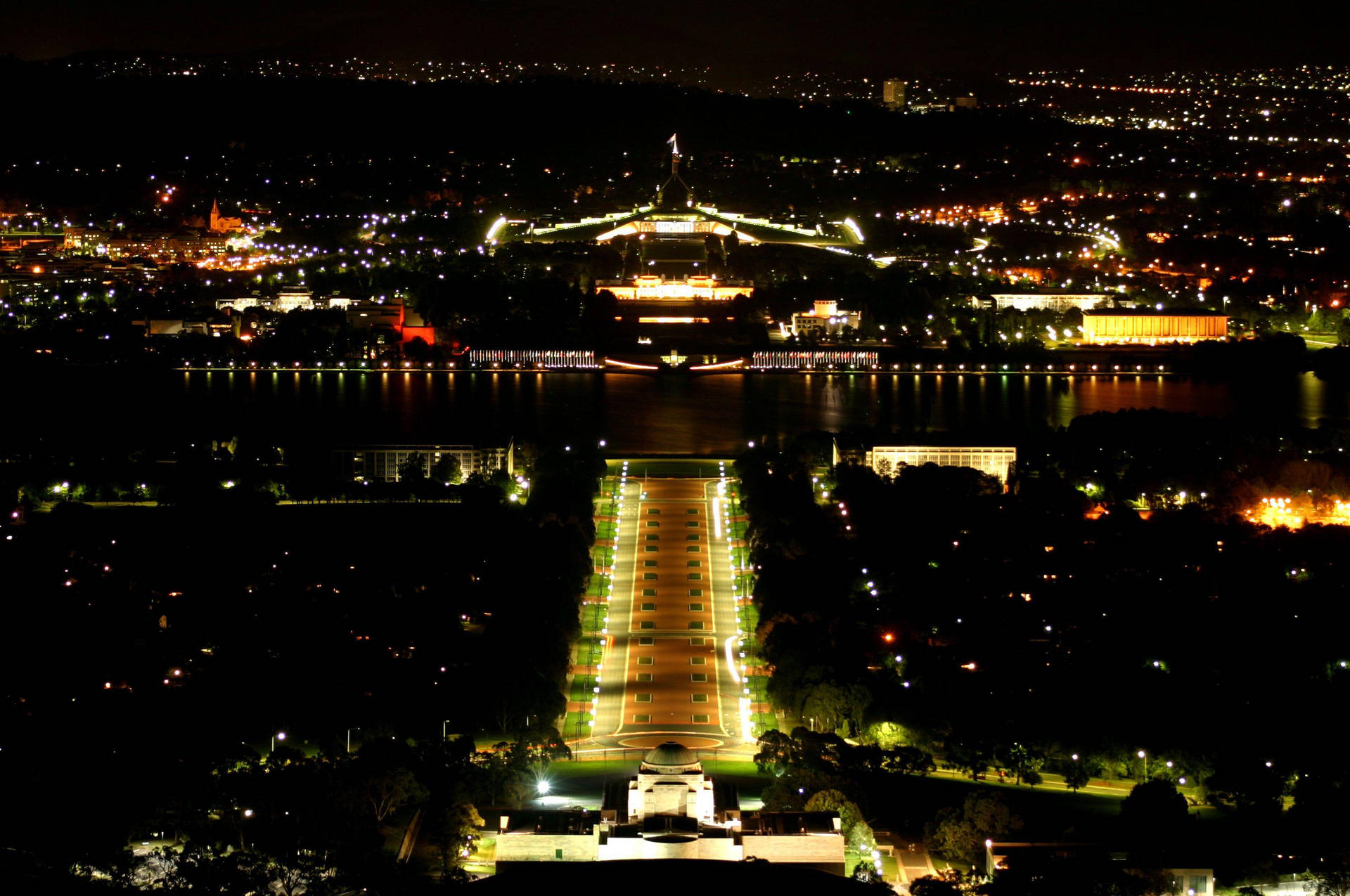坎培拉國會大廈和戰爭紀念館在夜間亮燈，湖中倒影。