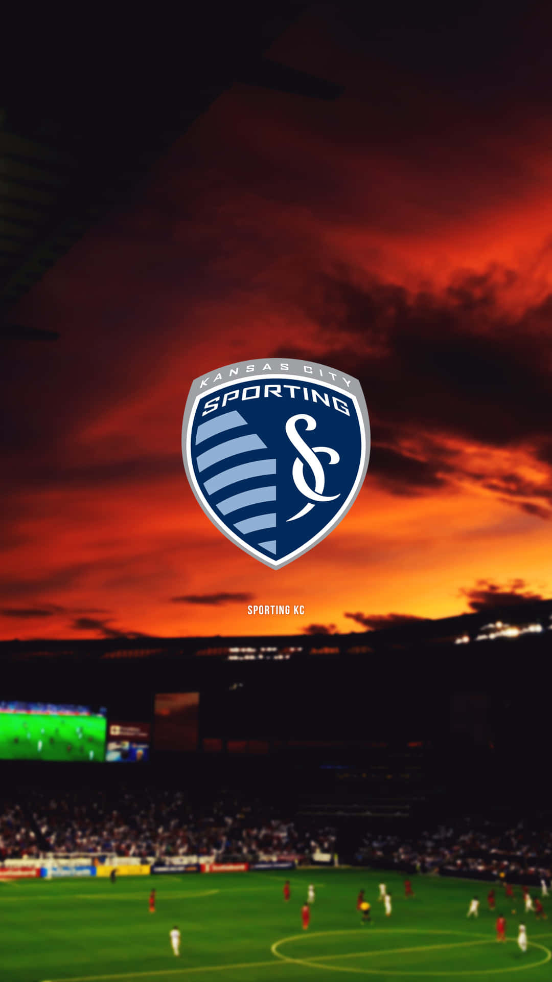 堪薩斯城競技隊主場球場的日落美景 壁紙 — Sporting KC 標誌居中，背景是黃昏時分擠滿人的足球場上空熾熱的日落天空。
