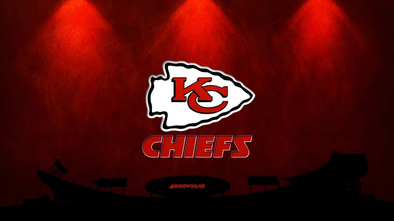 Kansas City Chiefs 桌布 壁紙 — 堪薩斯城酋長隊標誌在黑暗的體育場背景下被紅色聚光燈照亮，並可見「Arrowhead」。