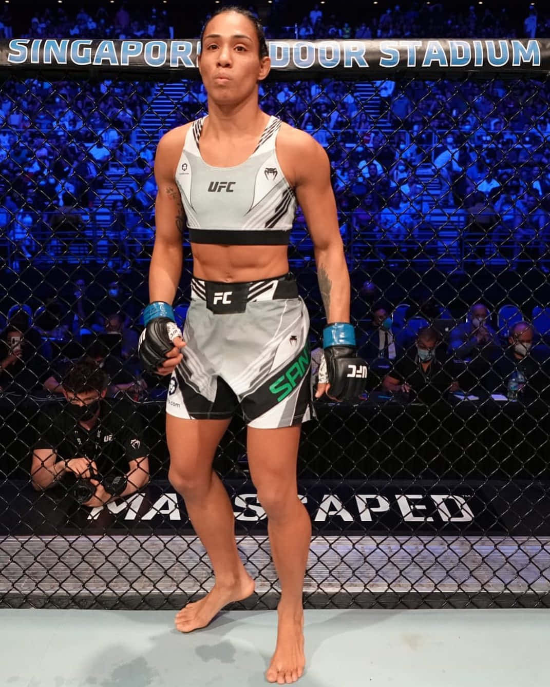 身穿UFC裝備的女性MMA拳手站在八角籠中，圍欄後有觀眾。