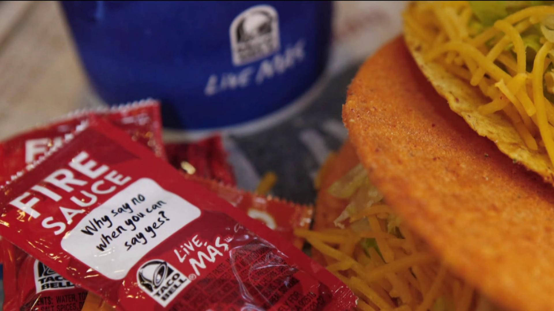 塔可鐘火辣醬 壁紙 — Taco Bell 火辣醬包和芝士玉米餅的特寫，背景有一個藍色飲料杯，呈現柔和焦點效果。