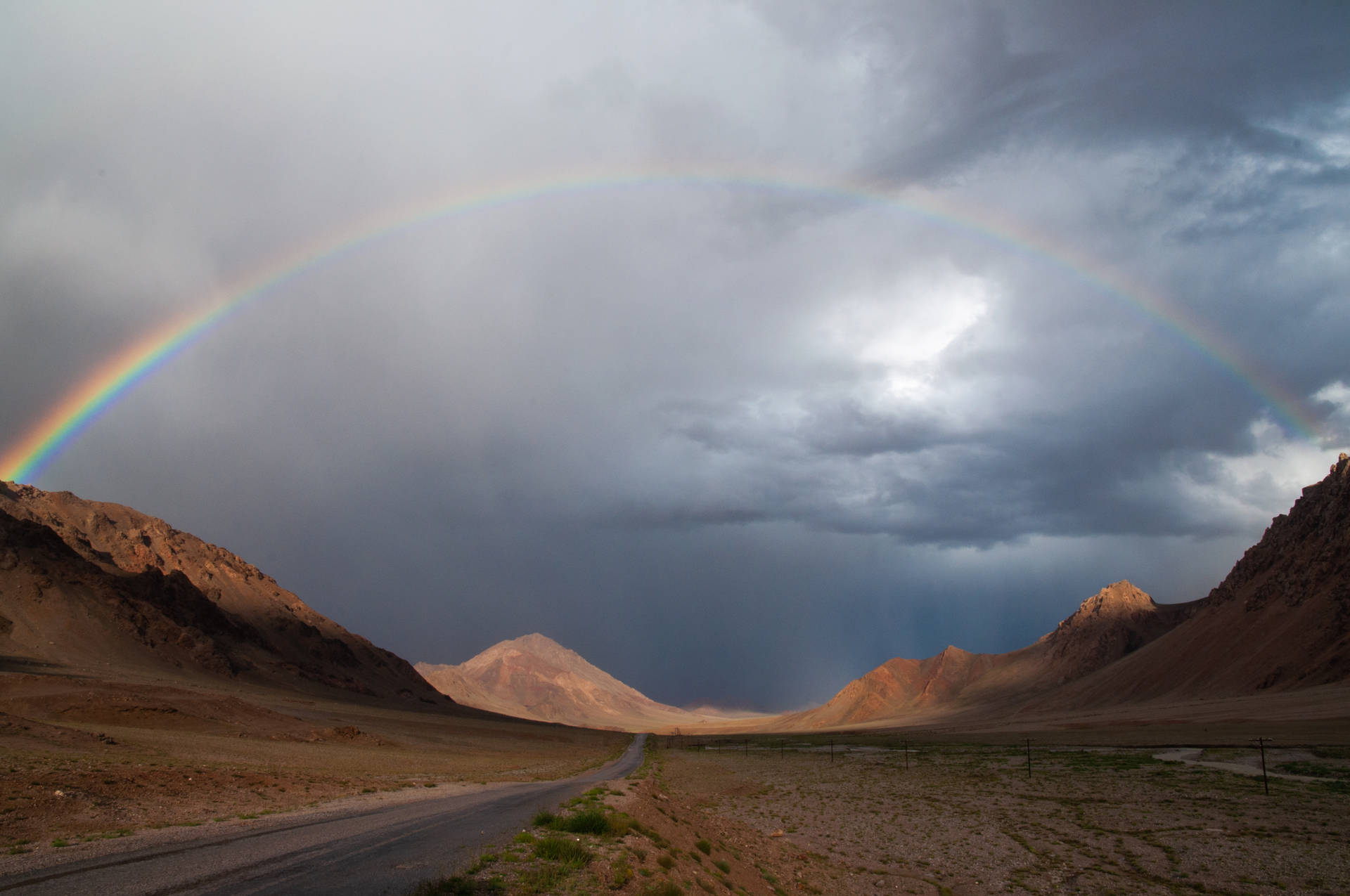 彩虹在沙漠景觀中的山路上方暴風雨的天空中延伸。