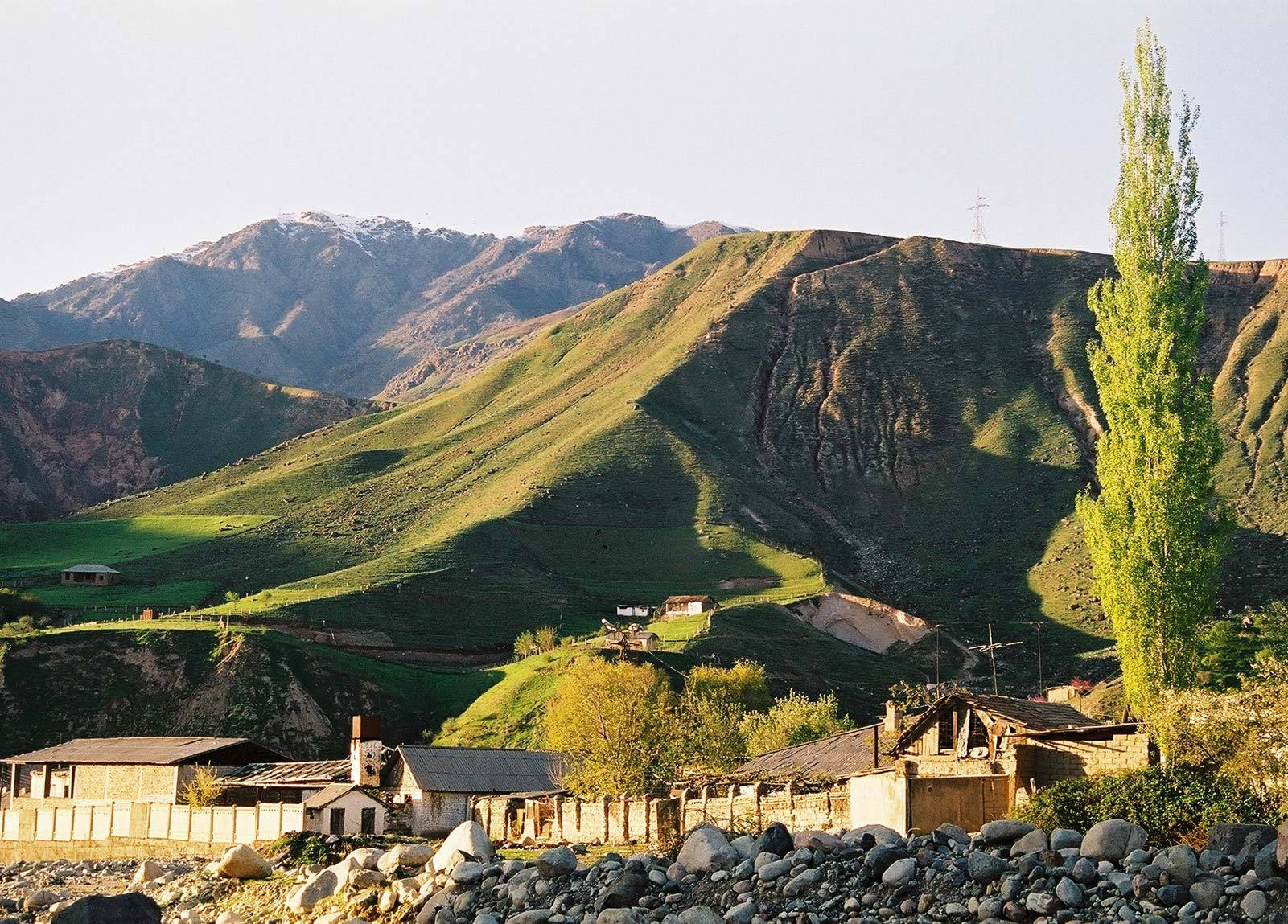 鄉村村莊坐落在綠色山谷中，有石屋和白雪覆蓋的山峰。