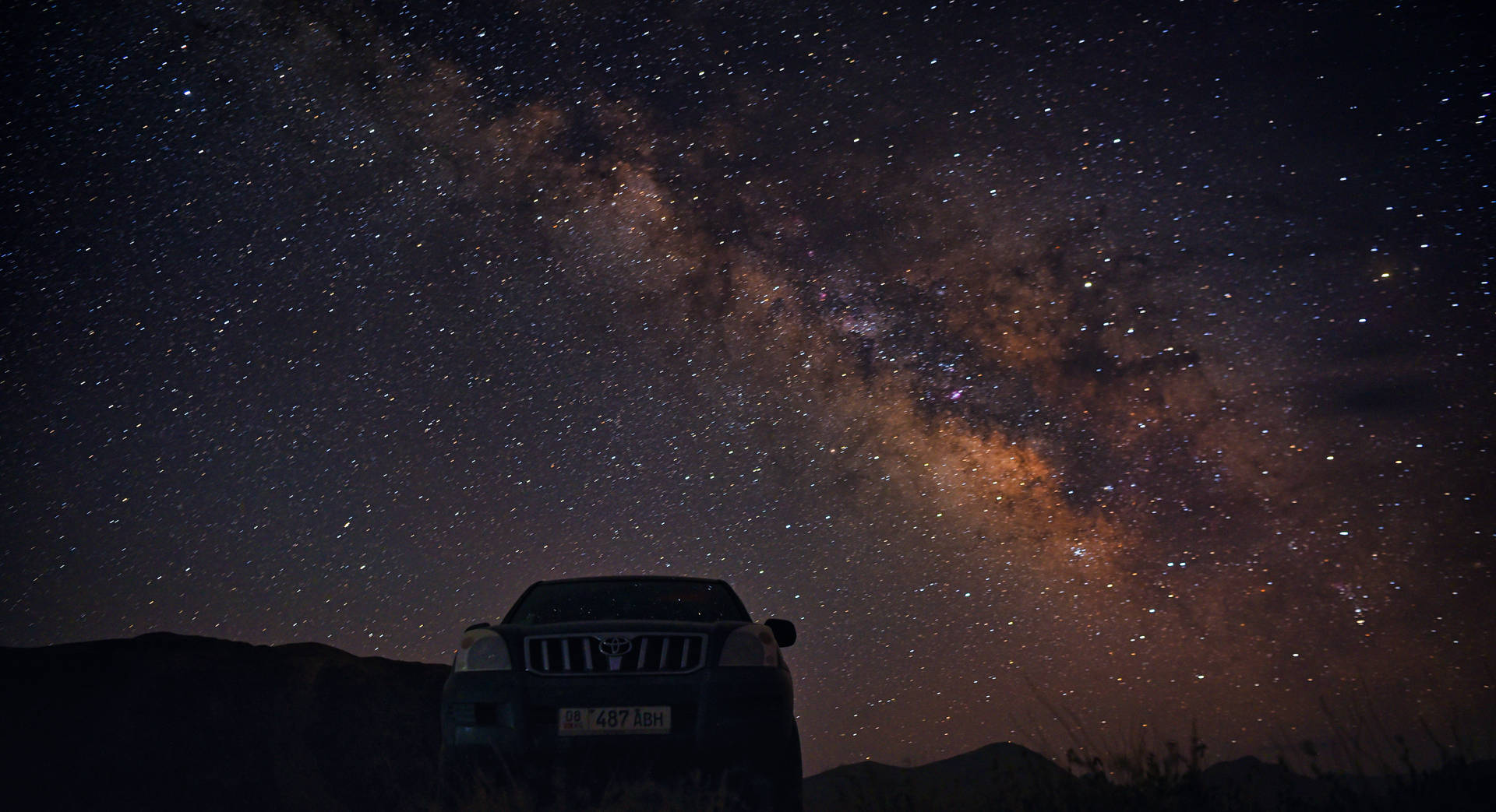 一輛汽車停泊在星空下，銀河清晰可見。