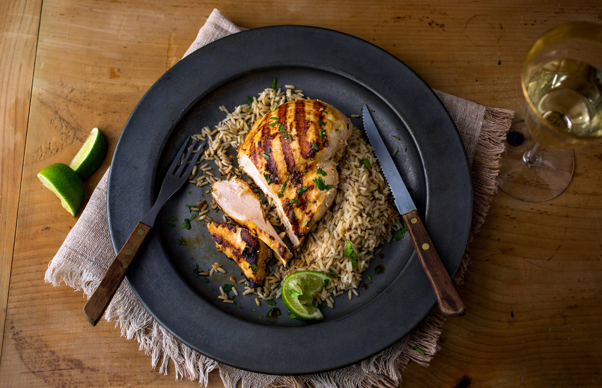 烤雞肉配飯和青檸，放在木桌上，附葡萄酒。