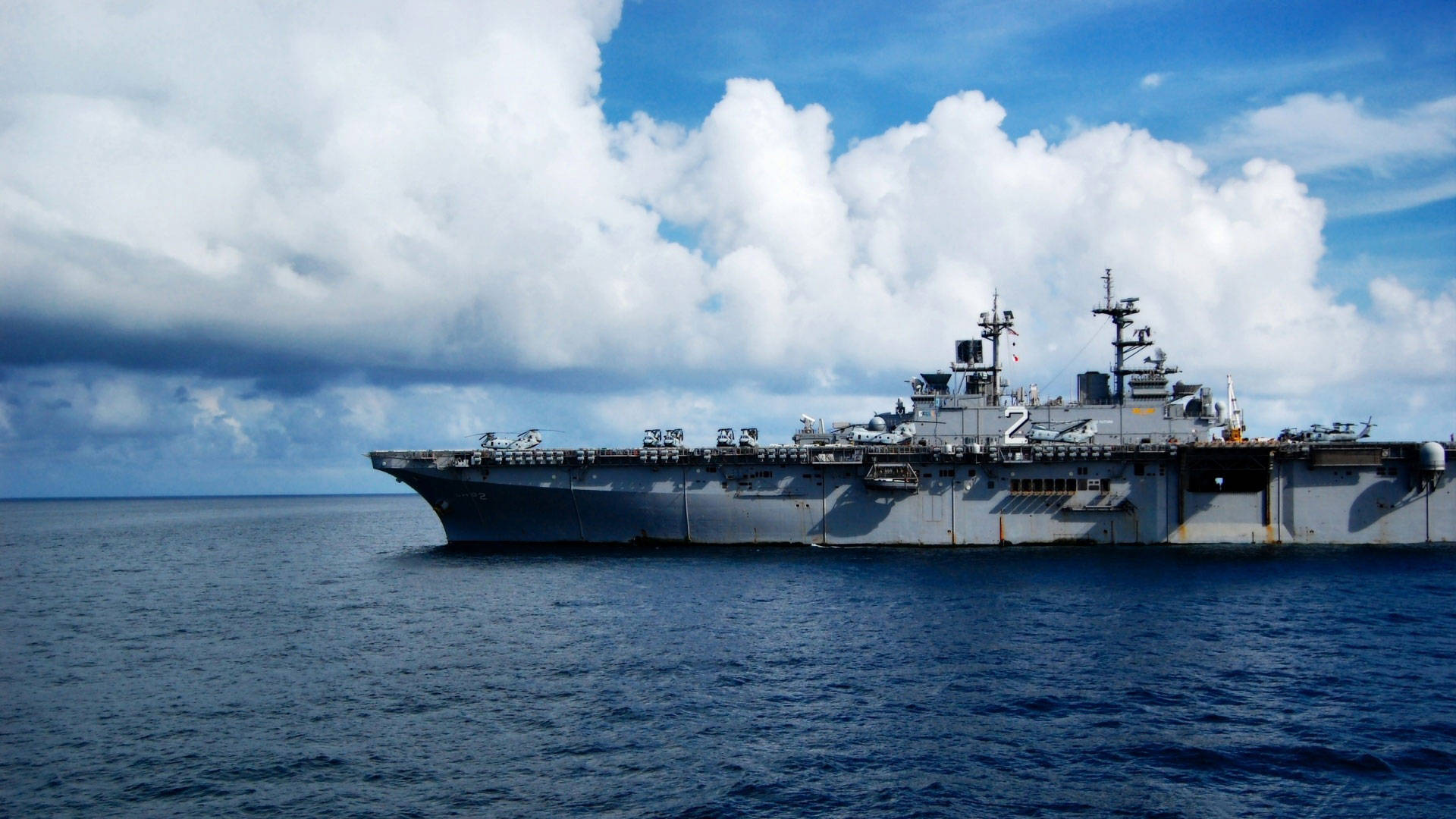 塗有灰色船體的戰艦 壁紙 — 一艘大型灰色航空母艦在深藍色海洋上平靜航行，天空佈滿蓬鬆的白雲，景象壯麗。