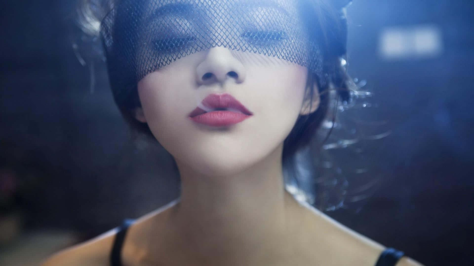 藍色燈光攝影棚中，紅唇女子戴著黑色面紗，伴隨著煙霧。