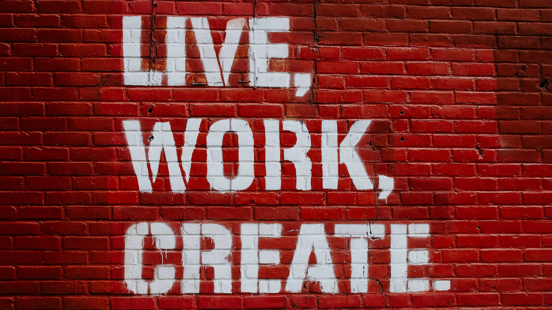 紅磚牆上白色油漆寫著 live work create。