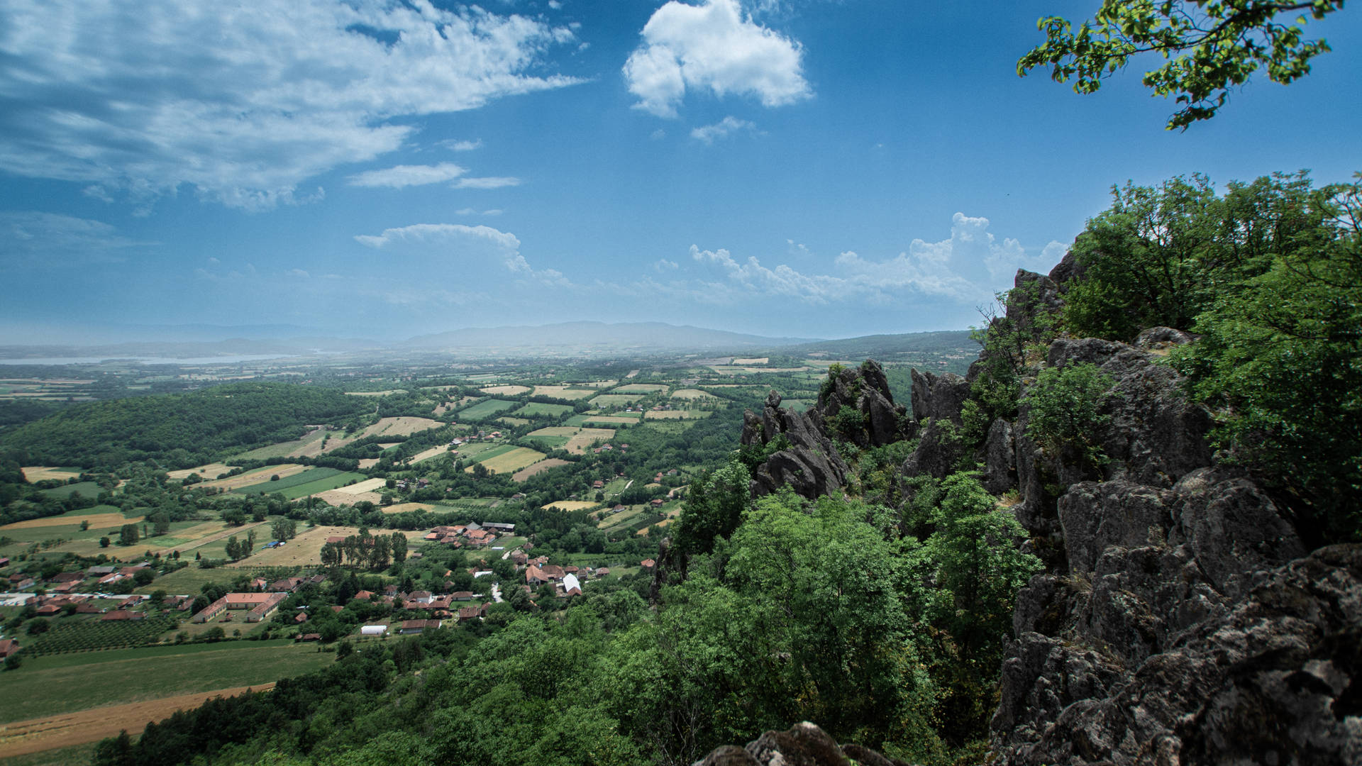 從岩石懸崖俯瞰的 panoramic 景觀，綠色山谷中有田野和村莊。