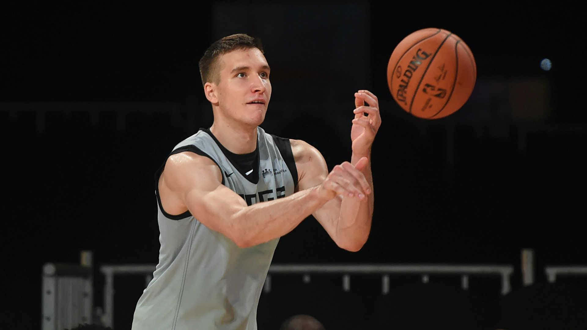塞爾維亞籍NBA球員波格丹·波格丹諾維奇 壁紙 — 一位專注的籃球運動員穿著灰色球衣，在黑暗的球場背景下準備投擲橙色 Spalding 球。