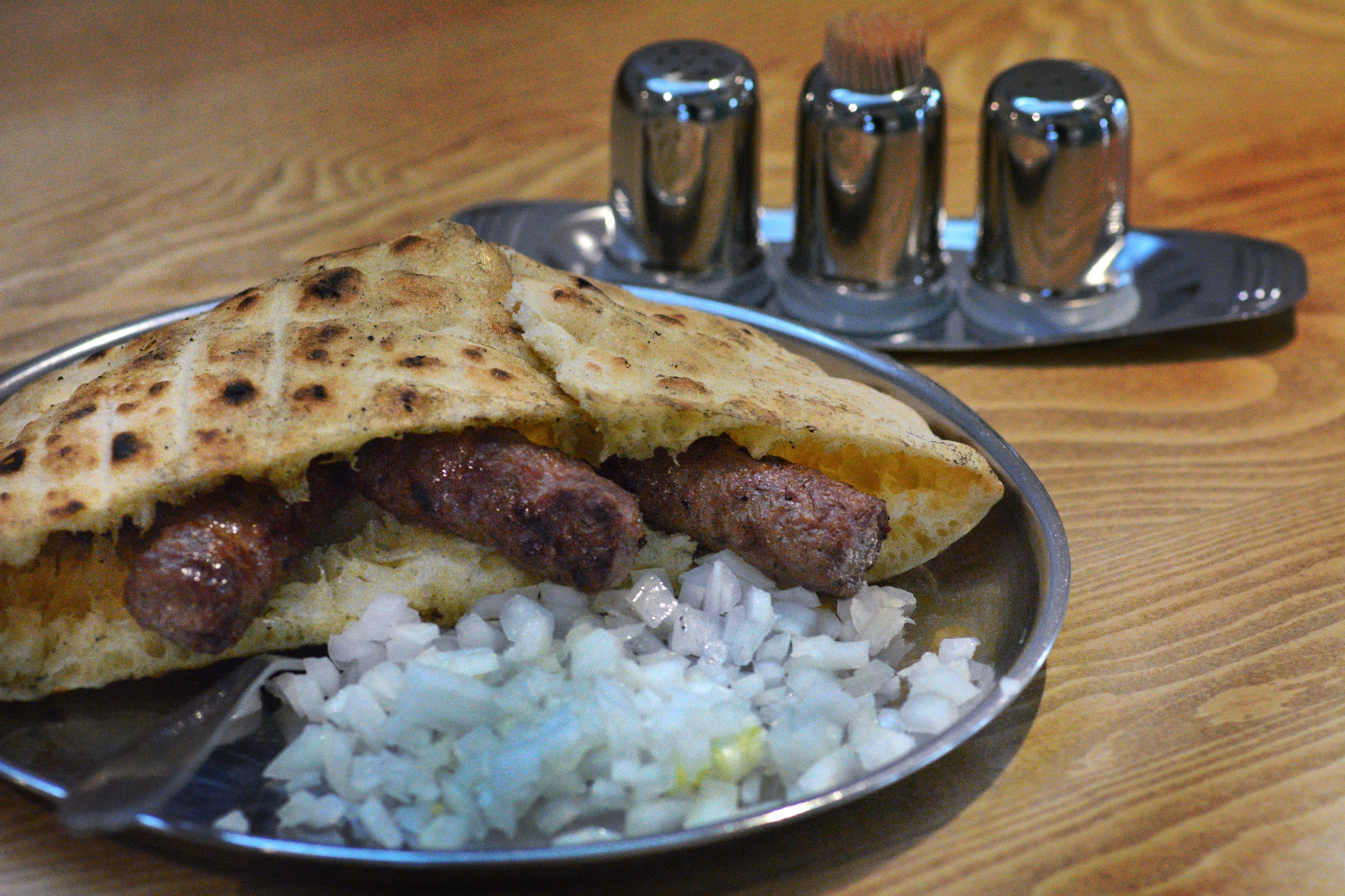 塞進皮塔麵包中的Ćevapi 壁紙 — 烤香腸三文治配以烤扁麵包，伴以切碎洋蔥，置於金屬碟上。
