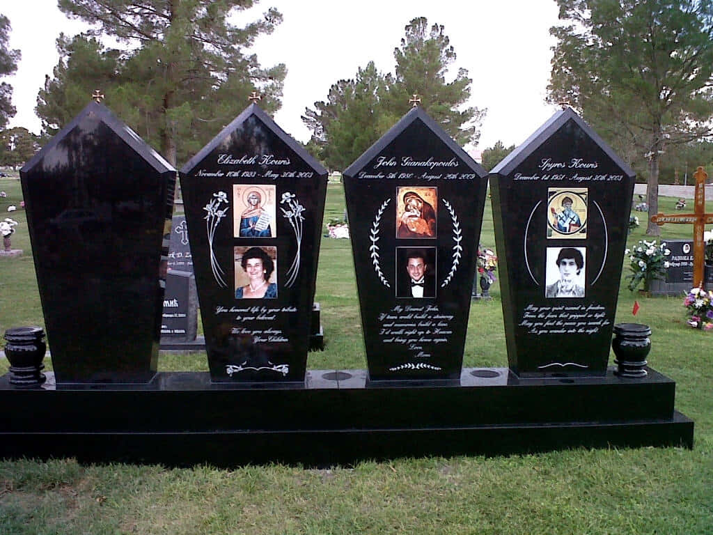 Memorial 桌布 壁紙 — 墓地裏的四塊黑色棺材形墓碑，每塊都展示著刻有照片和姓名的逝者，周圍環繞著綠草和樹木。