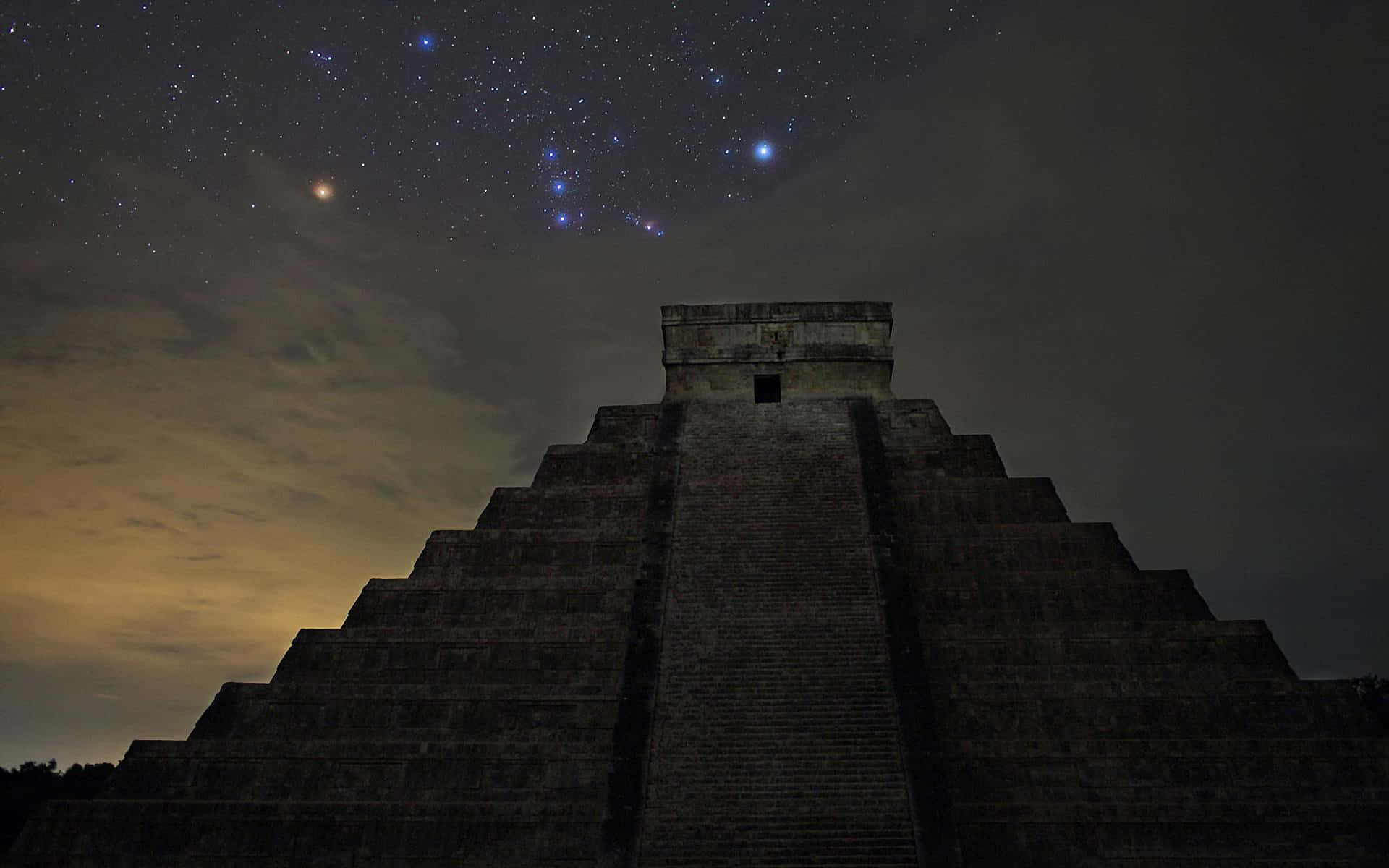 墨西哥奇琴伊察城堡藍色繁星夜景 壁紙 — 古老石金字塔在繁星點點的夜空下呈現剪影，可見星座和發光的地平線。