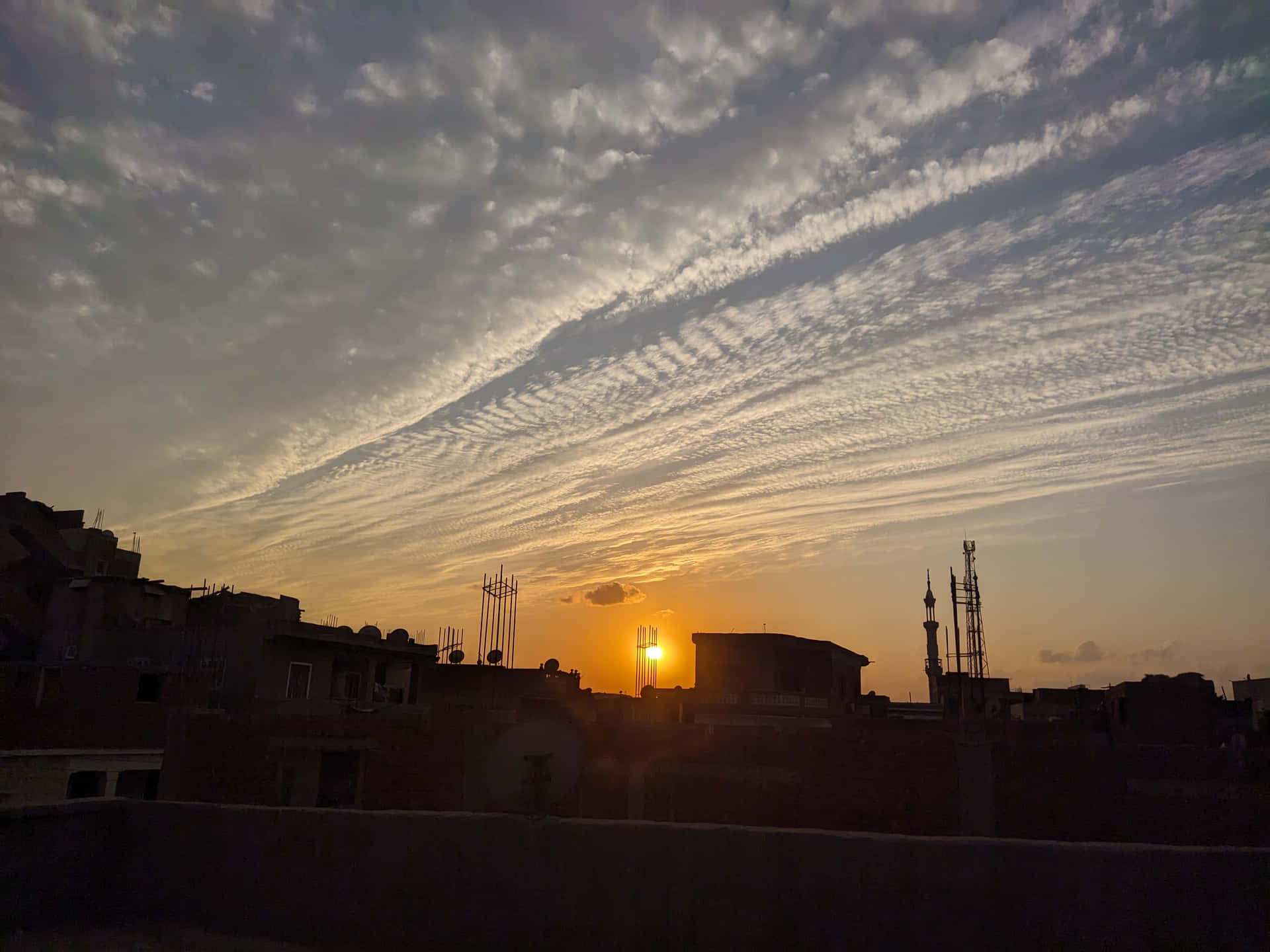 夕陽映照城市屋頂，宣禮塔與薄雲點綴橙色天空