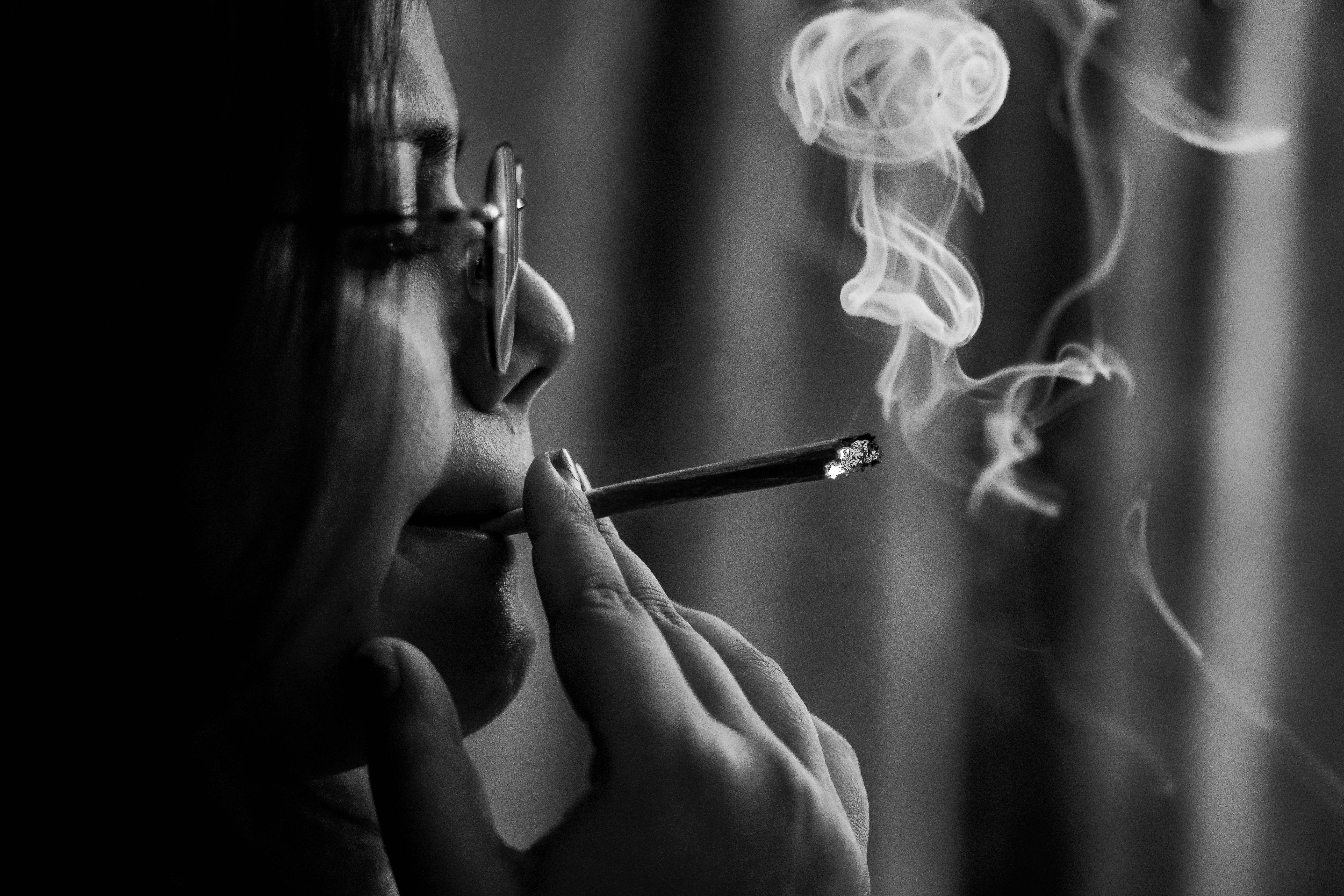 壓力下吸大麻 壁紙 — 一個人側面抽煙，煙霧向上繚繞，背景是模糊的窗簾，呈單色調。