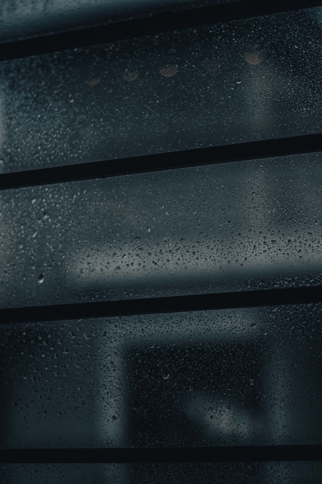 玻璃窗上的雨滴，帶有水平條框和背後模糊的城市燈光。