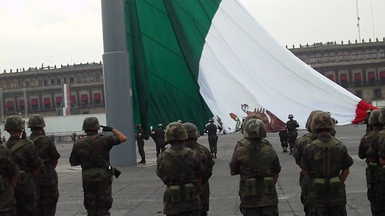 士兵向墨西哥國旗敬禮 壁紙 — 身穿迷彩軍服的士兵立正站好，一面巨大的墨西哥國旗在宏偉的新古典主義建築前展開。