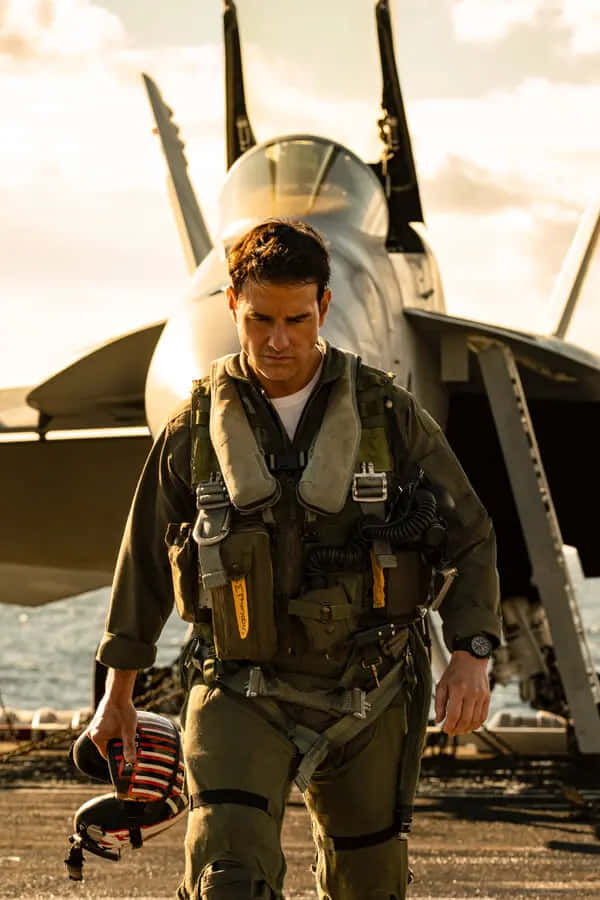 身穿飛行裝備的機師在日落時走向航空母艦甲板上的戰鬥機 — 頂尖飛行員： Maverick 壁紙