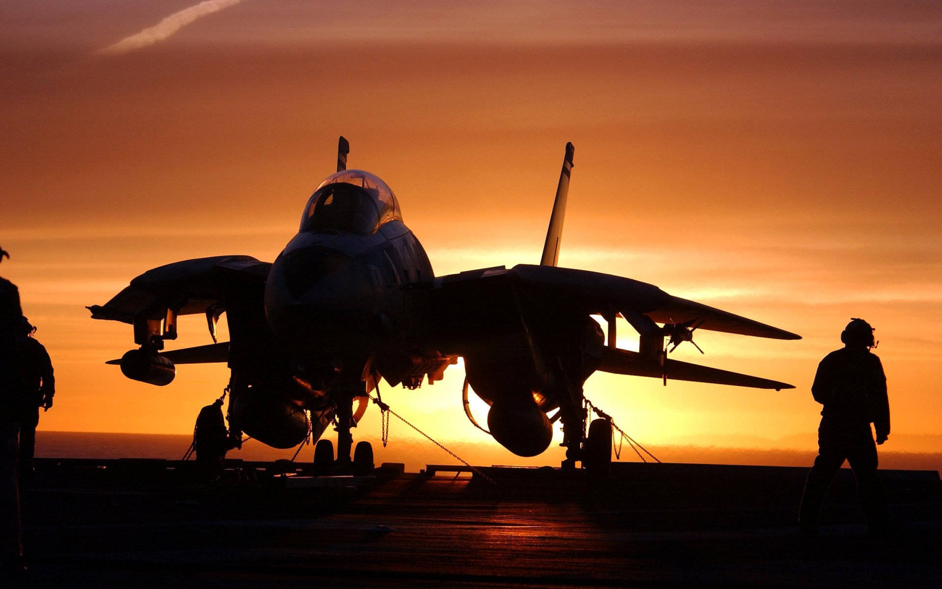 橙色日落中，航空母艦甲板上的戰鬥機剪影與船員。