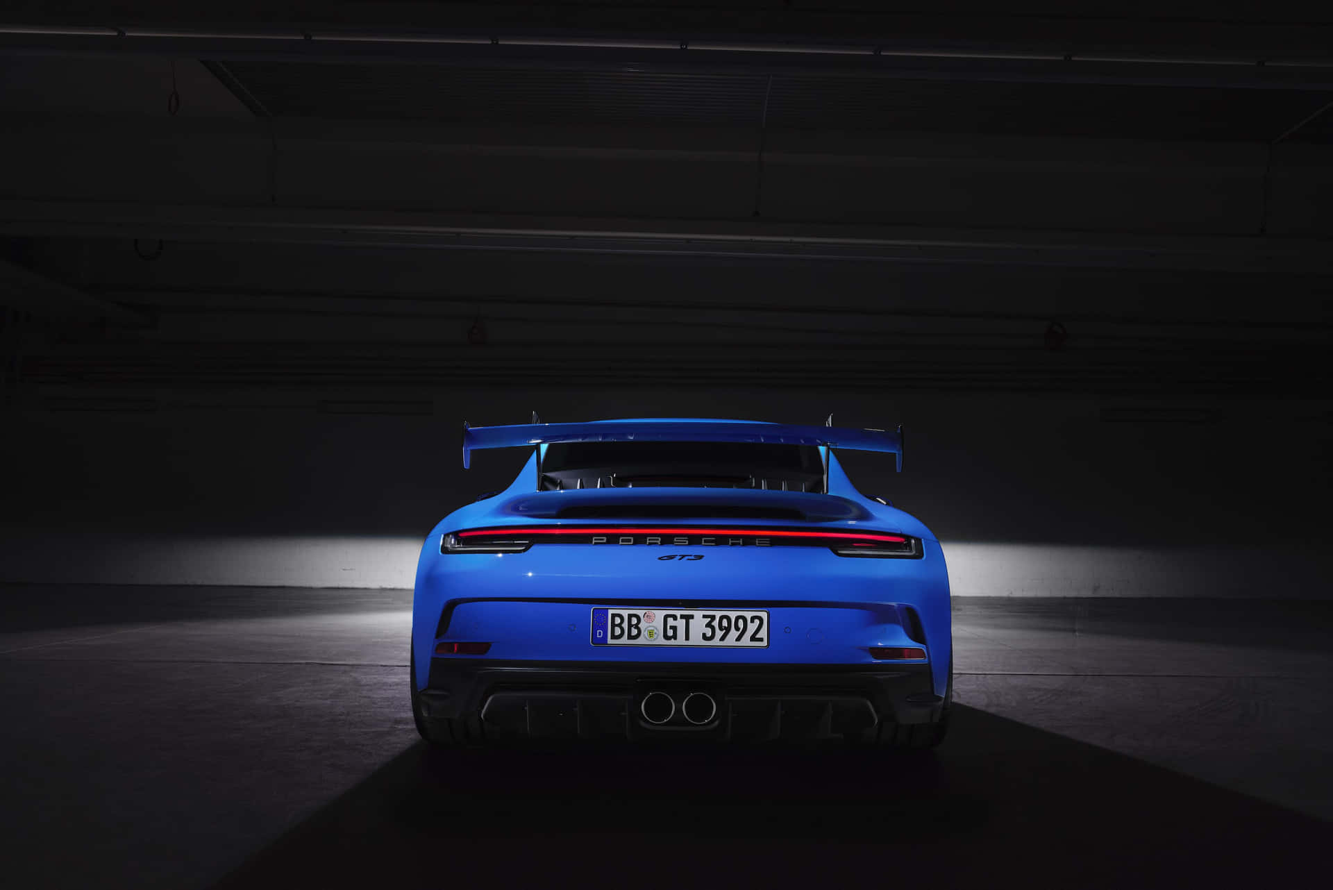 藍色保時捷911 GT3 RS在昏暗車庫中聚光燈下的後視圖。