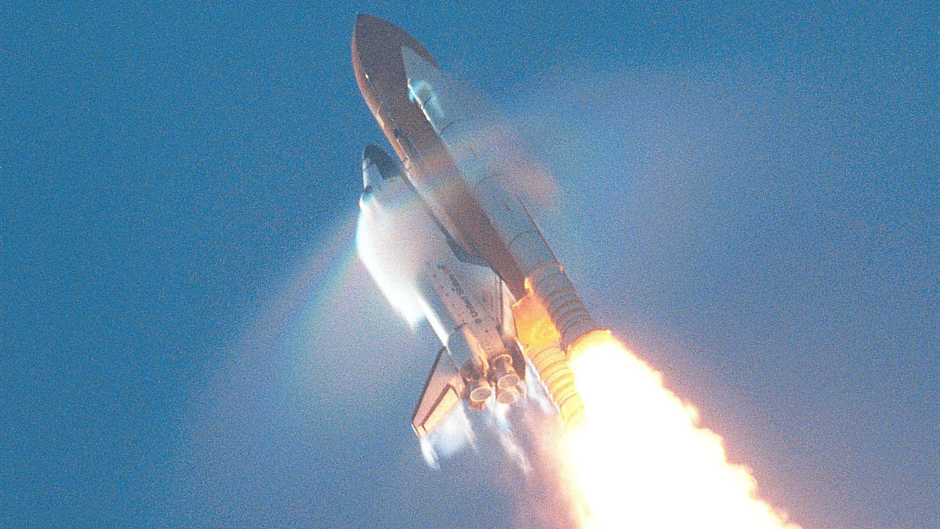 太空穿梭機在晴朗的藍天背景下以熾熱引擎發射升空。