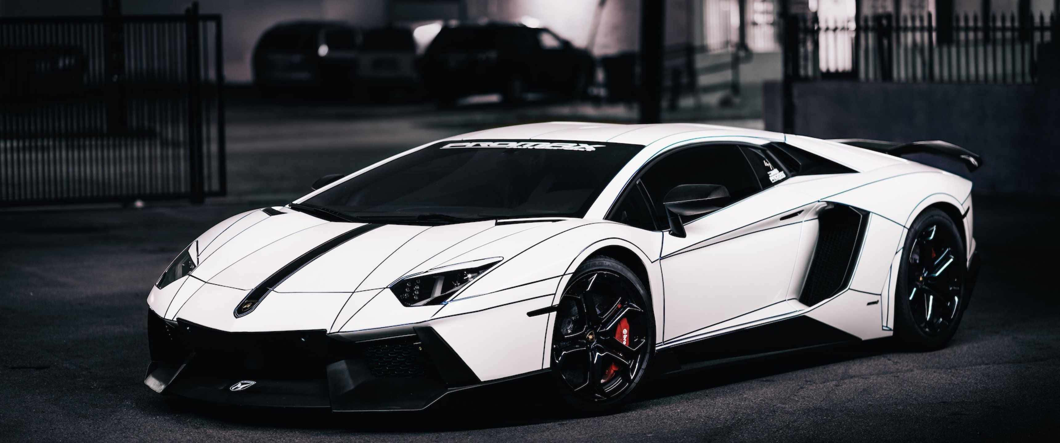 壯觀的 3440x1440p 蘭博基尼 壁紙 — 一輛時尚的白色林寶堅尼Aventador，帶有黑色飾邊和紅色制動卡鉗，停放在光線昏暗的城市車庫中。