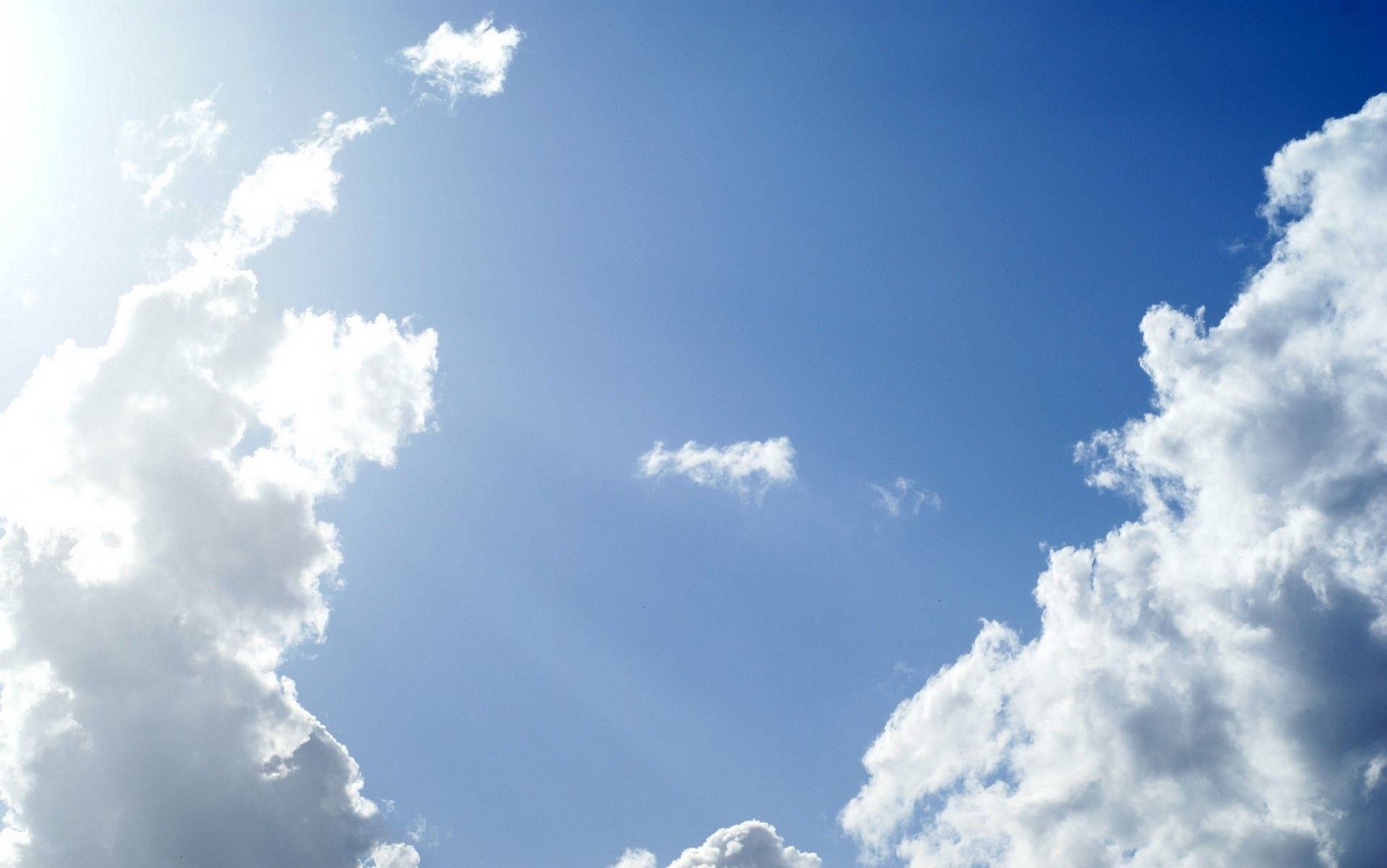 「壯觀的天空景色」 壁紙 — 鮮豔的藍天被蓬鬆的白雲框住，明亮的陽光穿透而過。