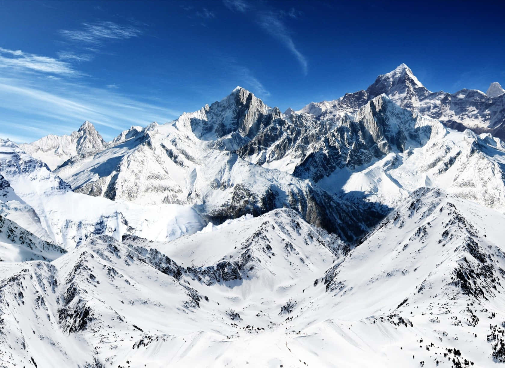 壯觀的雪山群峰美景 壁紙 — 白雪覆蓋的山峰刺穿鮮豔的藍天，薄雲在高山崎嶇地形上投下陰影。