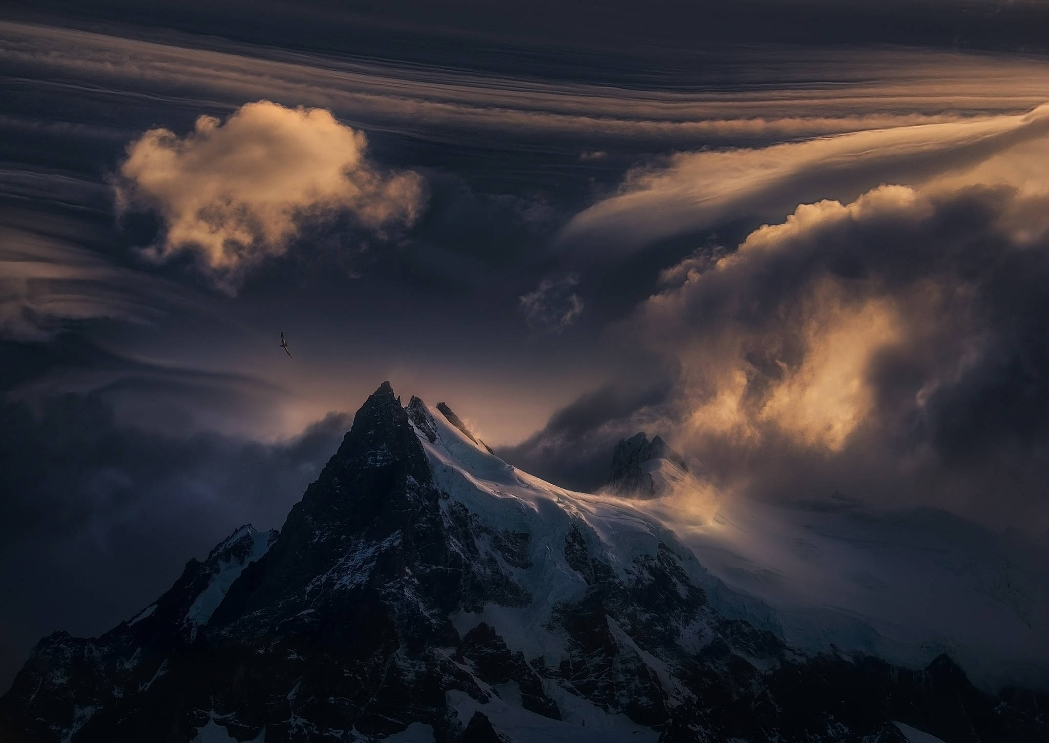壯觀雪山之巔 壁紙 — 白雪覆蓋的山峰刺穿被金色夕陽照亮戲劇性的雲層。