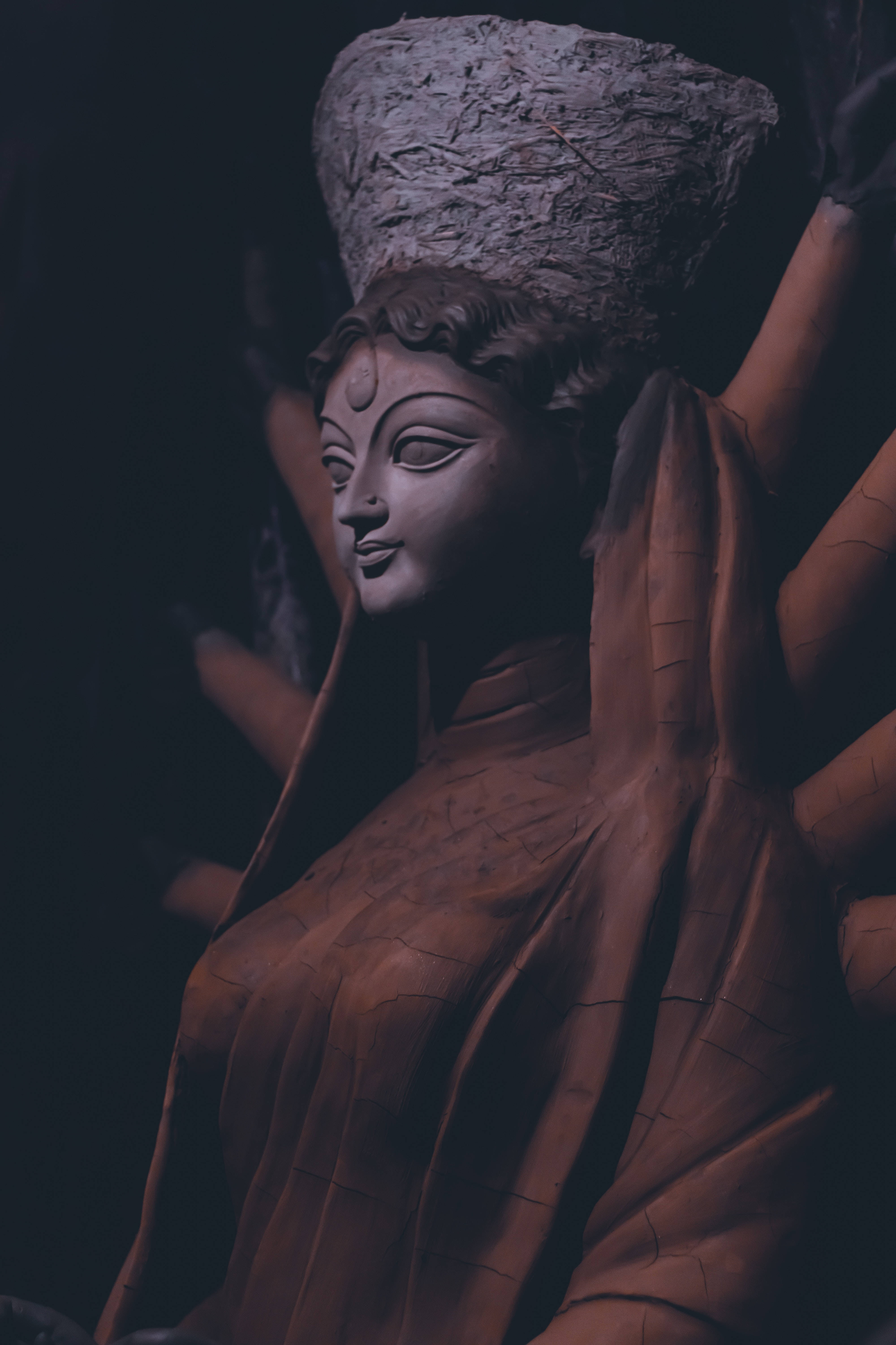 壯麗女神雕塑 壁紙 — 一尊寧靜的石像，神祇戴著紋理王冠，身披垂墜長袍，在黑暗背景中由柔和的方向性光線照亮。