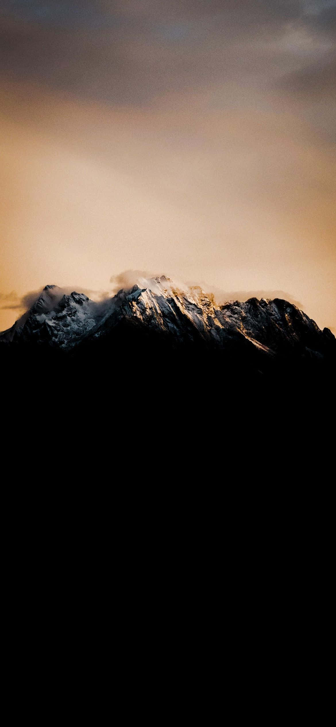 驚艷山峰 壁紙 — 白雪覆蓋的山峰在溫暖的金色日落天空襯托下形成剪影，上方有烏雲。