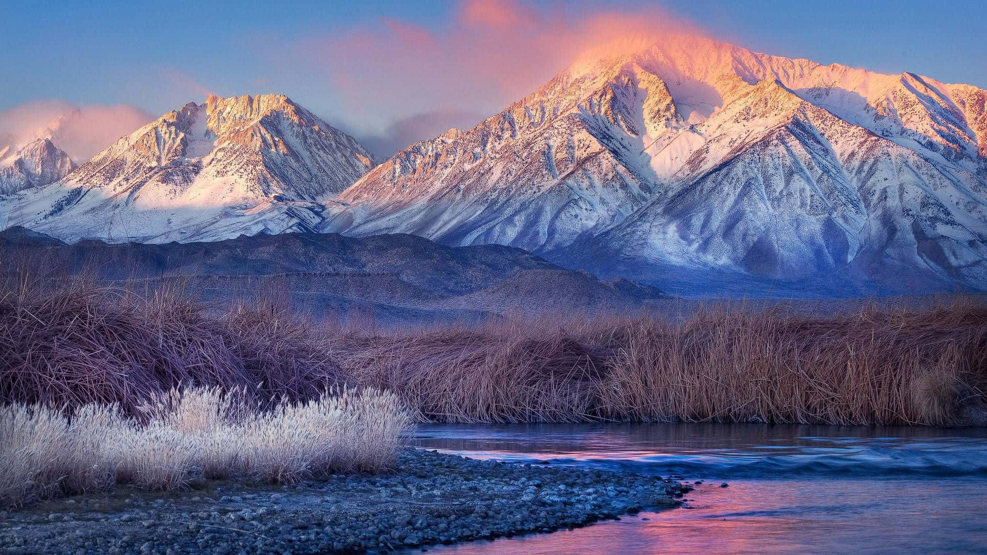 壯麗山景 壁紙 — 積雪的山峰在日出時閃耀著粉紅色和金色，河流在結霜的蘆葦下倒映著天空。