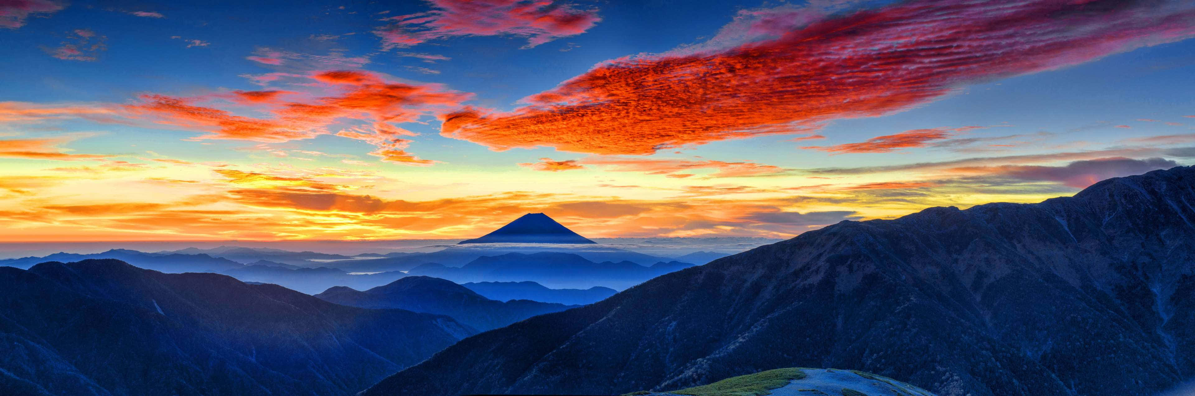 日落時分的富士山，藍色山脈上方有鮮豔的橙色雲彩。
