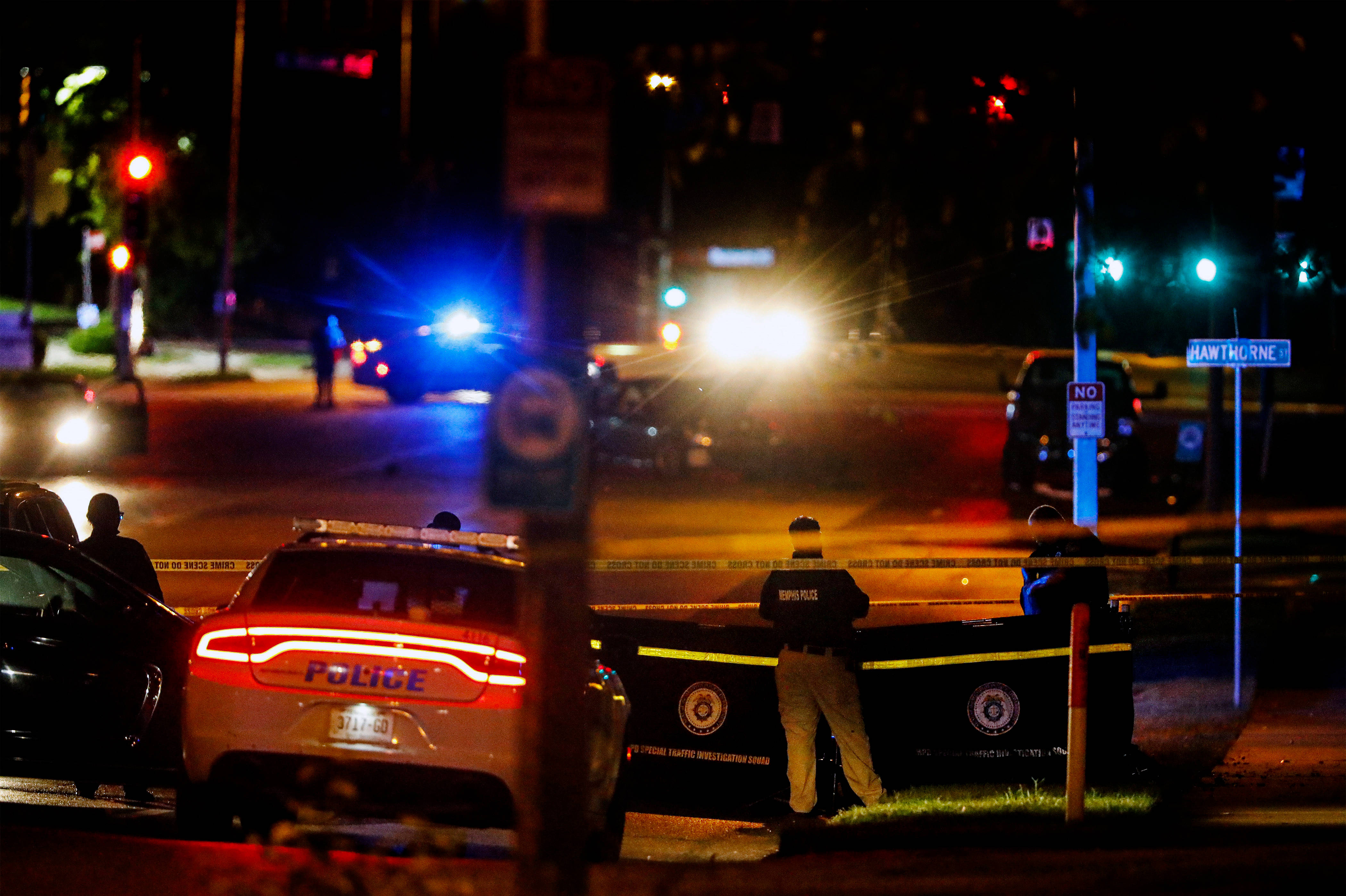 壯麗日落映照孟菲斯天際線 壁紙 — 警車閃著警燈，在夜晚的街燈和交通信號燈下包圍著犯罪現場。