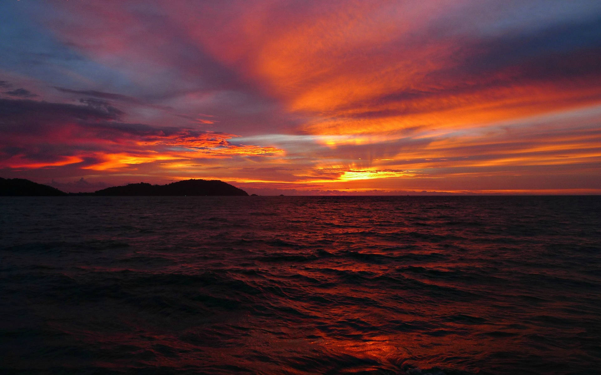 海洋上戲劇性的夕陽，剪影島嶼和熾熱的紅橙色天空。