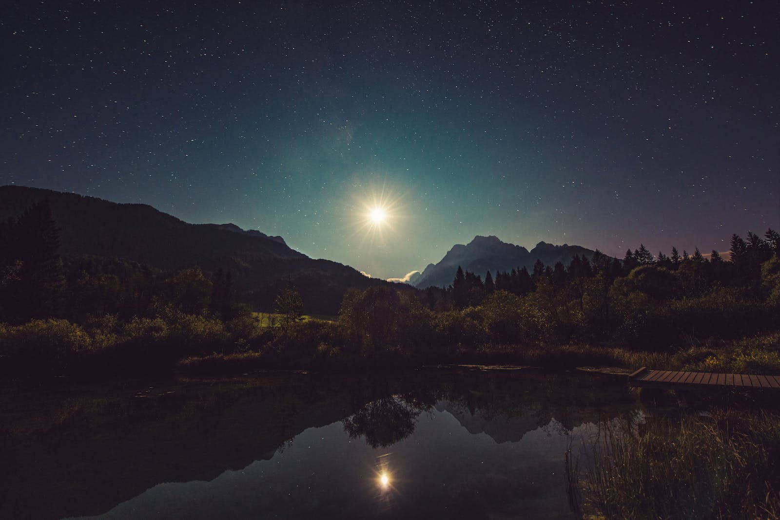 月光倒映在被山脈和樹木環繞的湖面上，星空下。