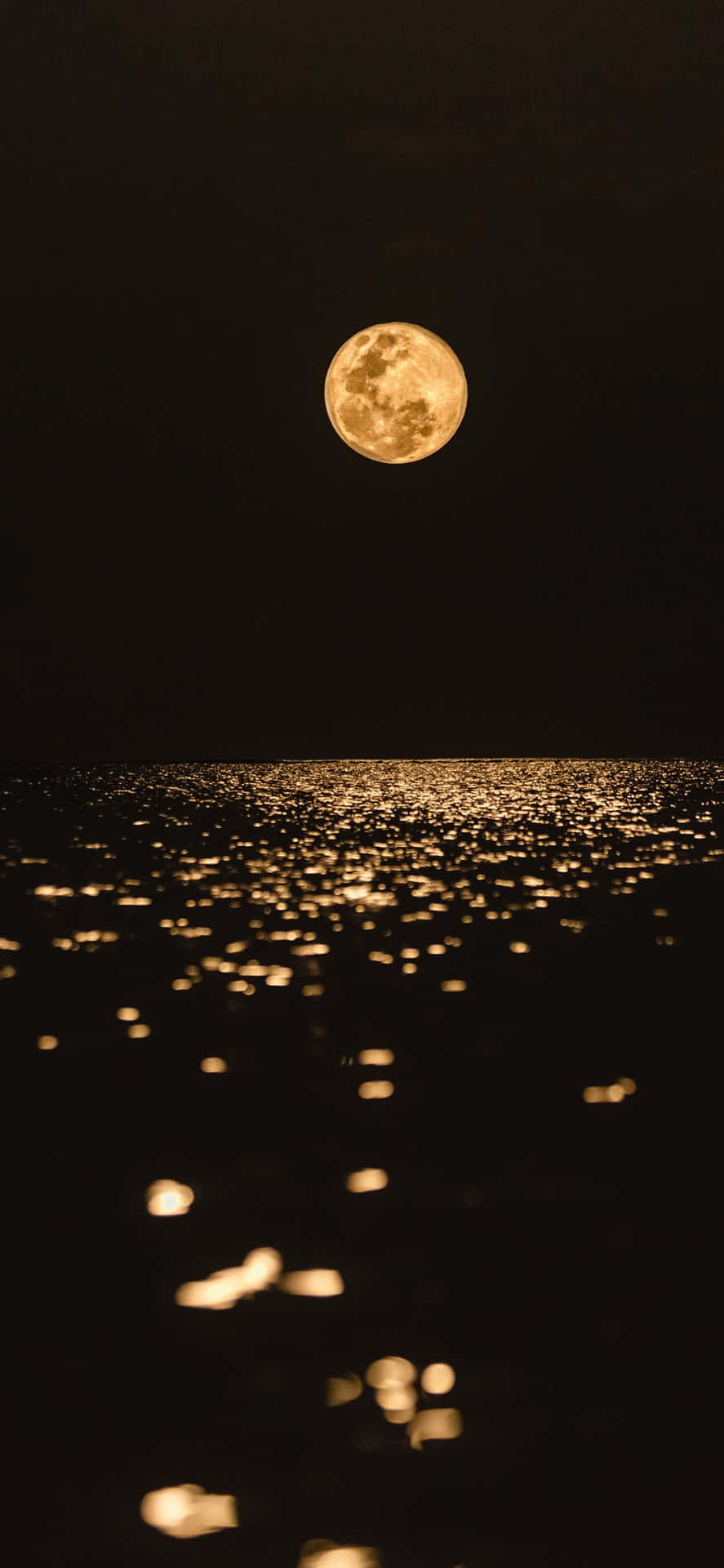 壯麗滿月對比夜空 壁紙 — 一輪明亮的滿月懸掛在黑暗的海洋上空，金色的光芒閃爍，散落的散景反射在水面上舞動。