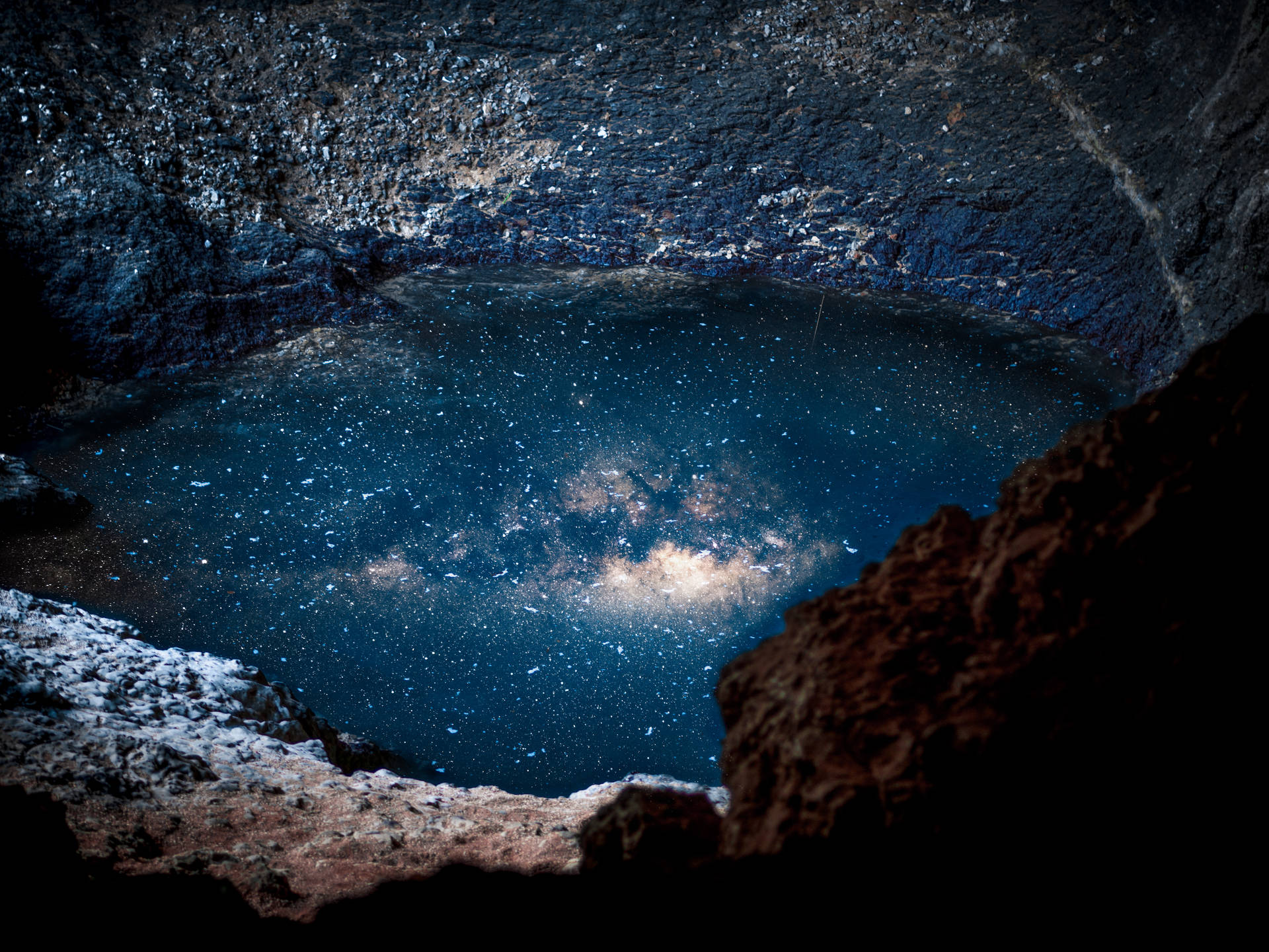 夜晚，星空倒映在岩石環繞的黑暗水池中。