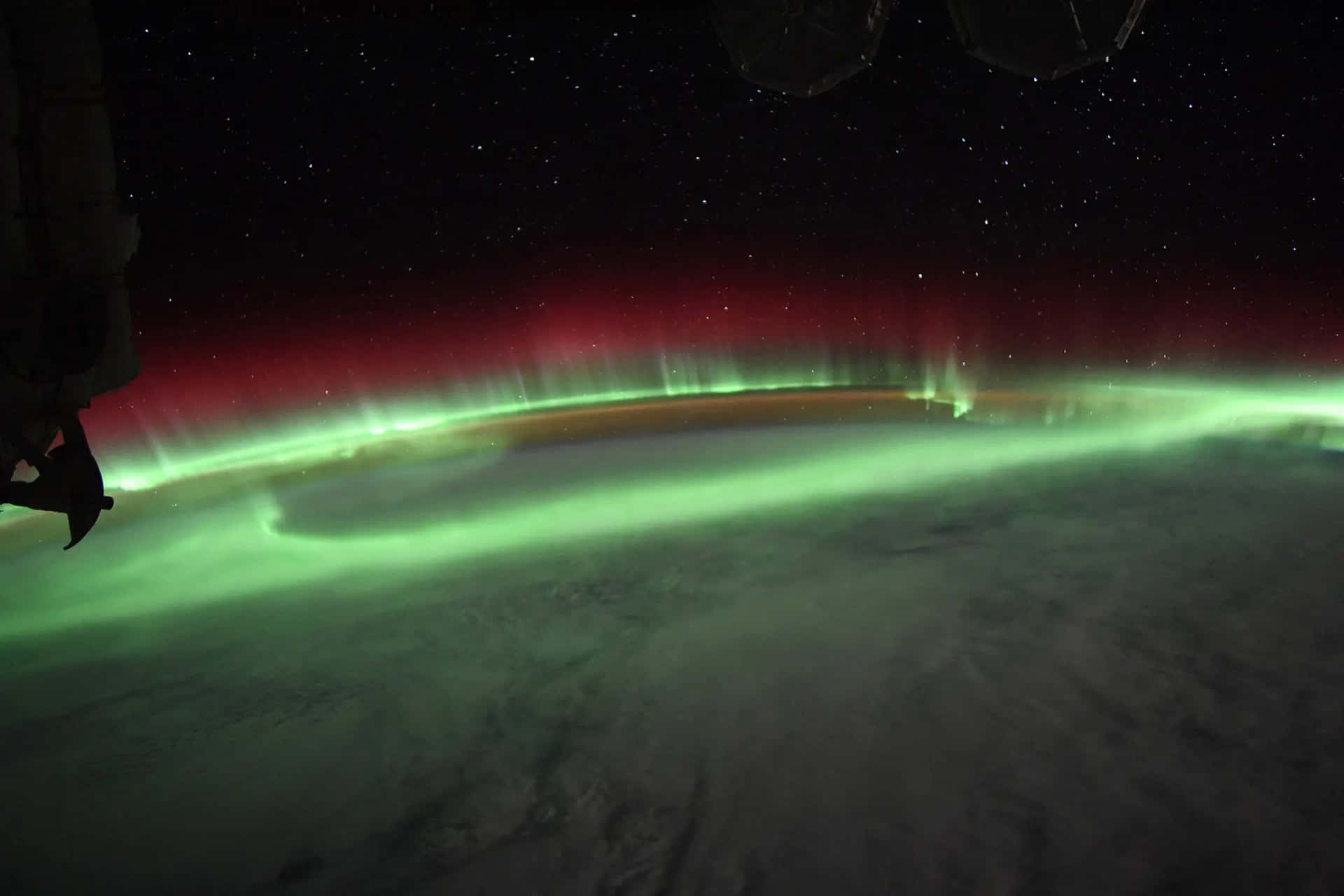 極光從太空在地球上空發出綠色和紅色的光芒，背景有星星。