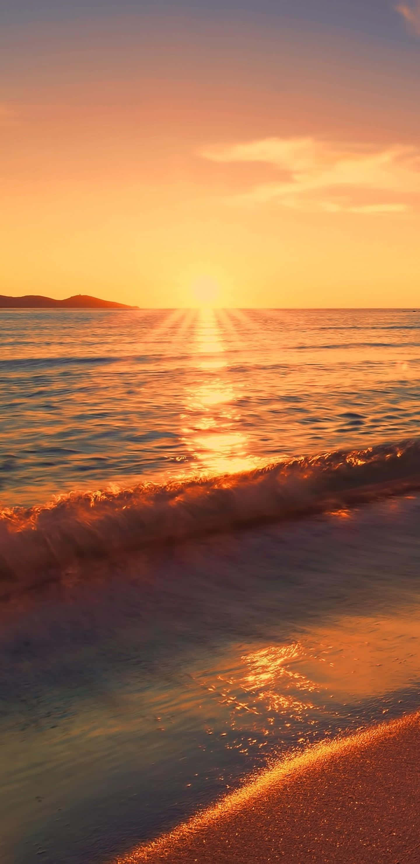 壯麗的海岸日落 壁紙 — 金色夕陽在平靜的海面上投射出耀眼的光芒，溫柔的海浪輕吻著沙灘，遠方的山丘呈現出剪影。