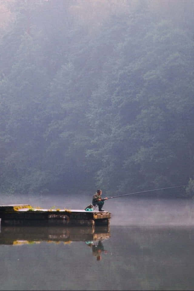 漁夫從霧氣瀰漫的碼頭在平靜的湖泊上釣魚，周圍是森林。