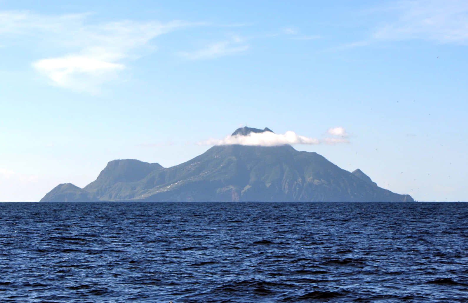 一座綠色的山島，山頂附近有雲，位於藍色海洋的中間。