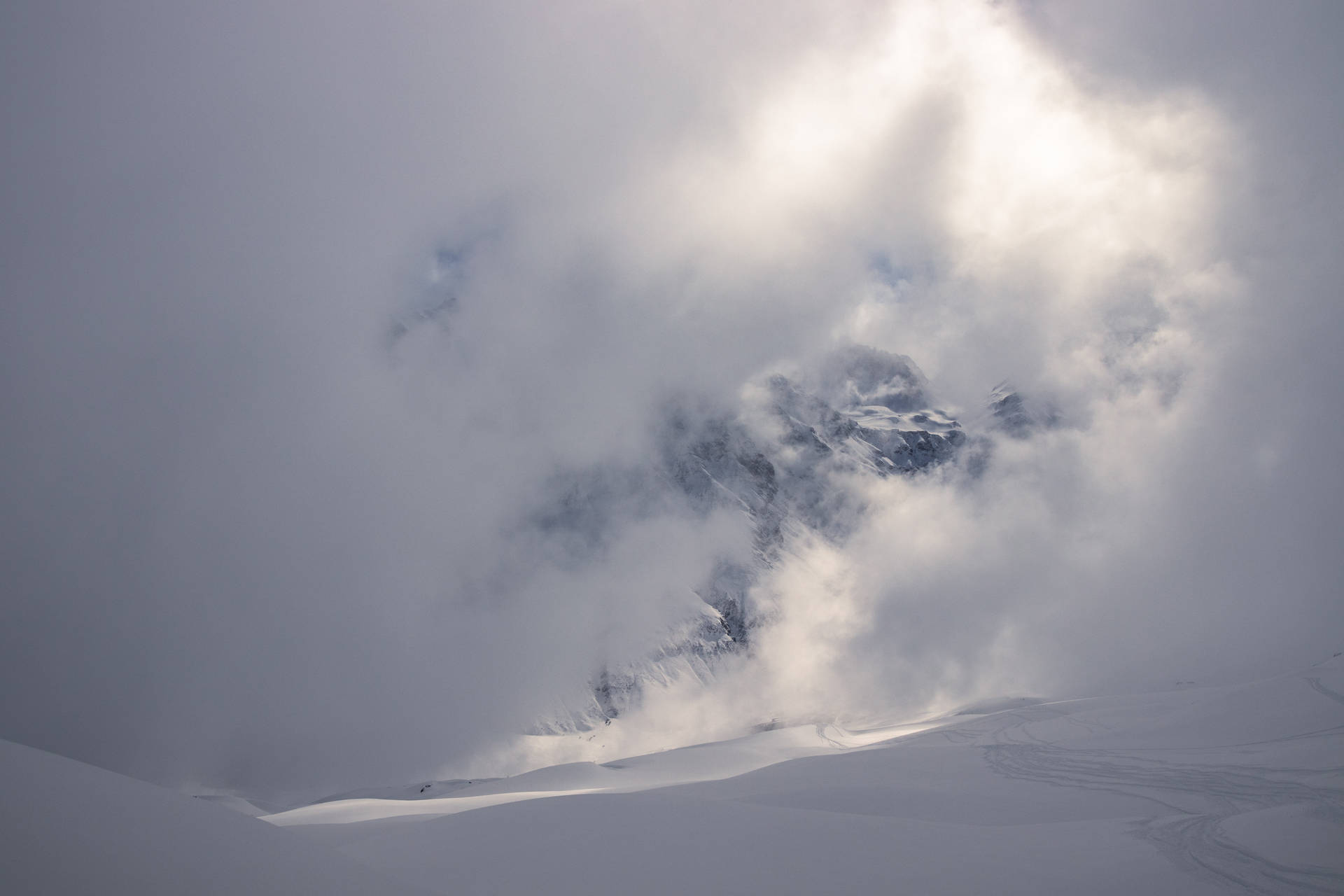 積雪的山峰穿破雲層，前景有滑雪痕跡。