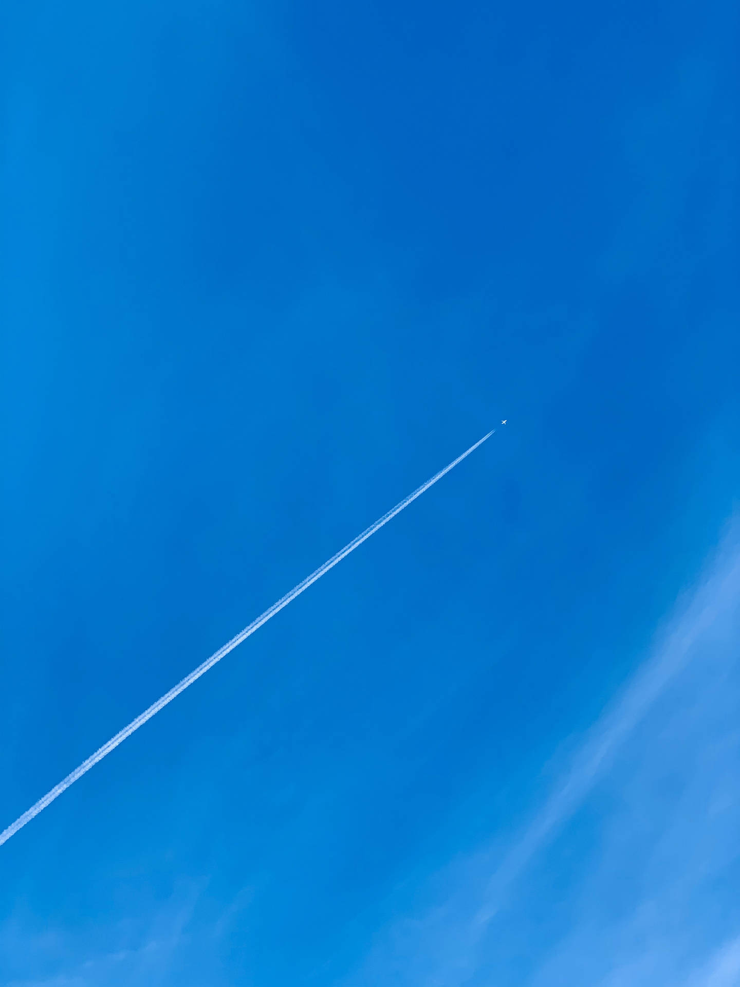一架小飛機在高空飛行，在明亮的藍天中留下一道長長的白色痕跡。